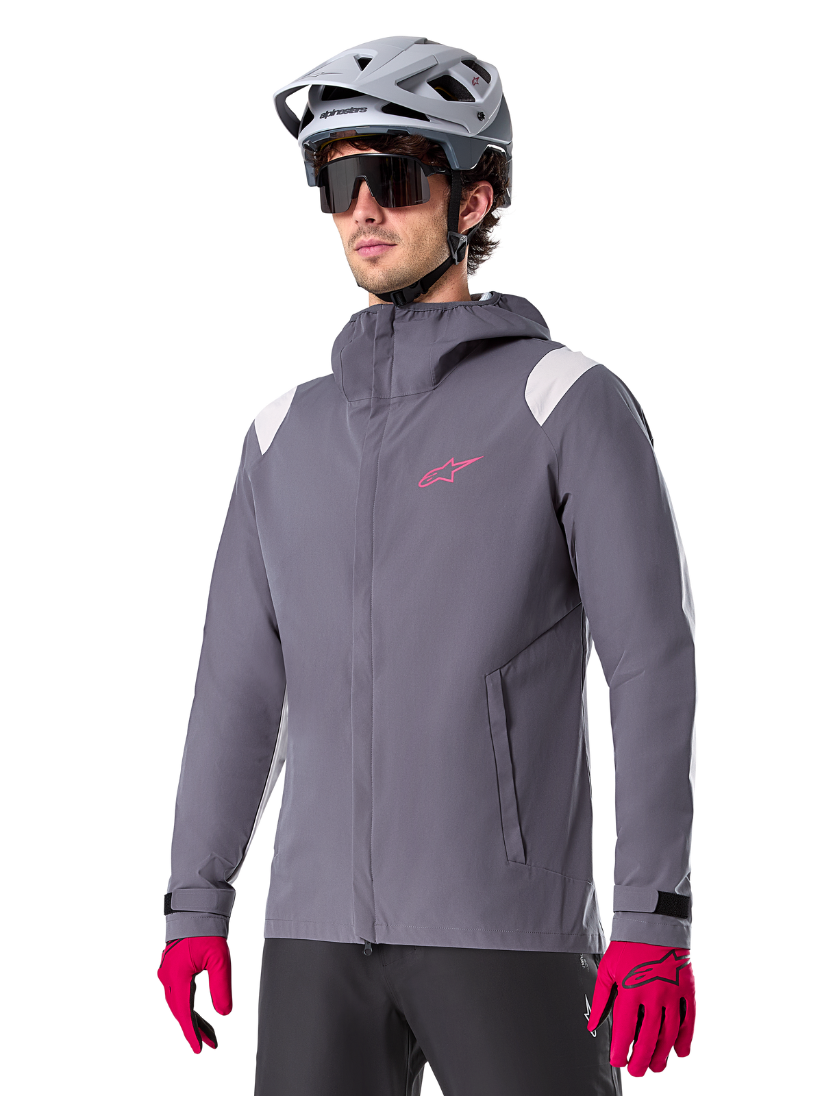 Alpinestars A-Dura Regenjas, mountainbike-regenjas, donker titanium grijs met roze logo en witte schouderaccenten, ontwerp met capuchon en voorzakken, gedragen met roze handschoenen en een lichtgrijze fietshelm