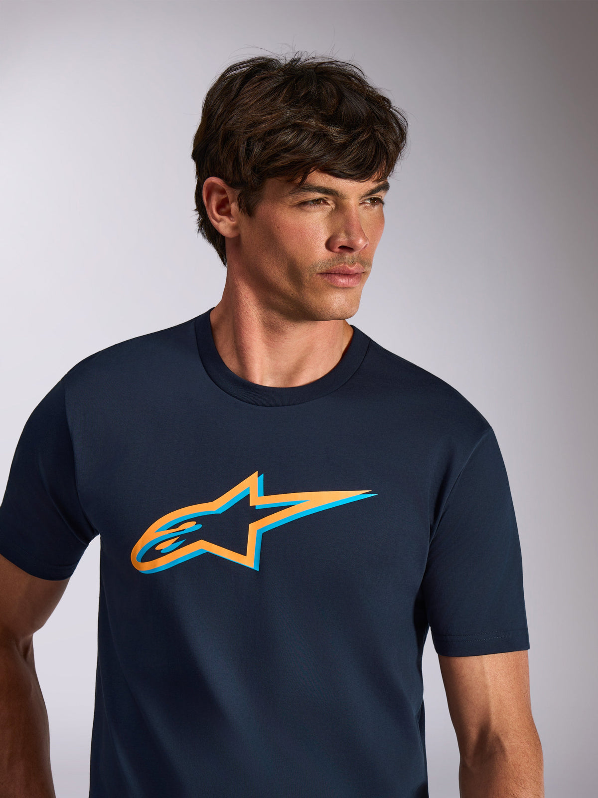 Alpinestars Ageless Shadow CSF Tee, T-shirt met korte mouwen, marineblauw met oranje en lichtblauw Astars-logo, casual motorsport streetwear, model draagt navy blauw shirt