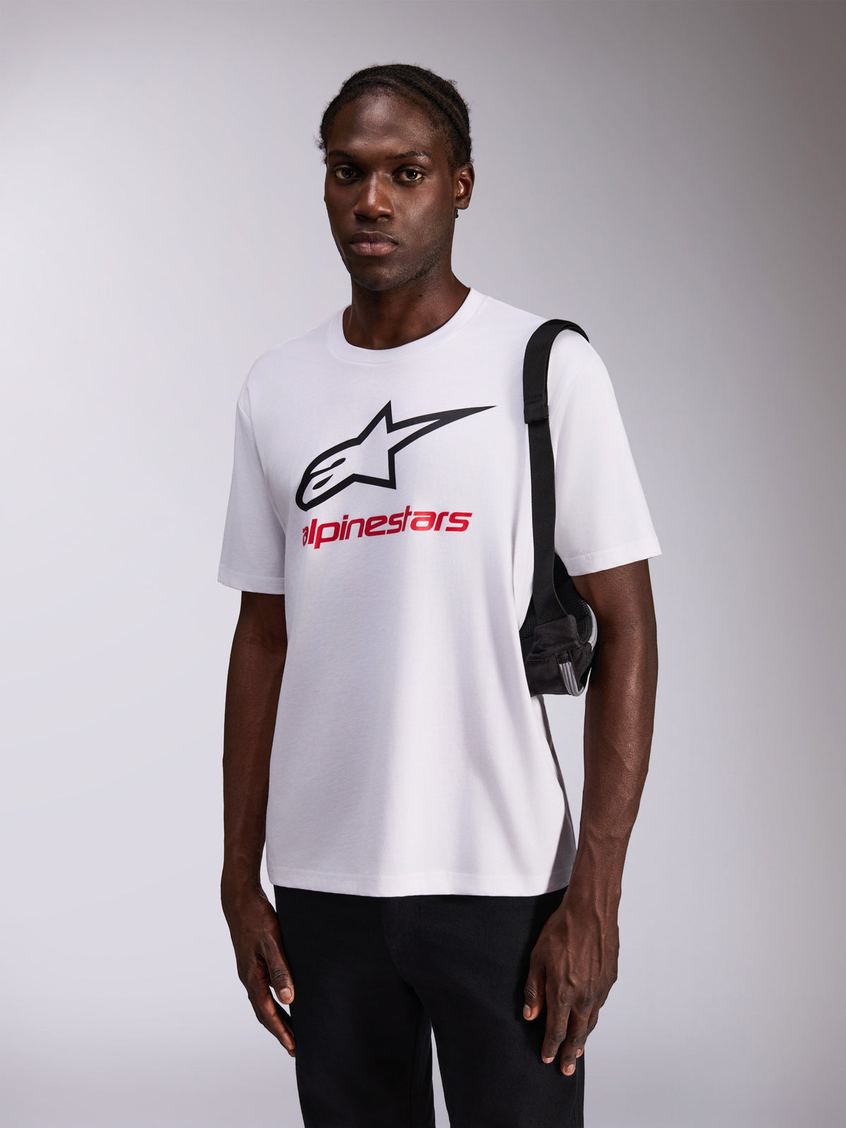 Alpinestars Always 2.0 CSF Tee, T-shirt met korte mouwen, wit met groot zwart sterlogo en rode merknaam, gedragen door model met zwarte broek en schoudertas, casual streetwear geïnspireerd op de motorsport