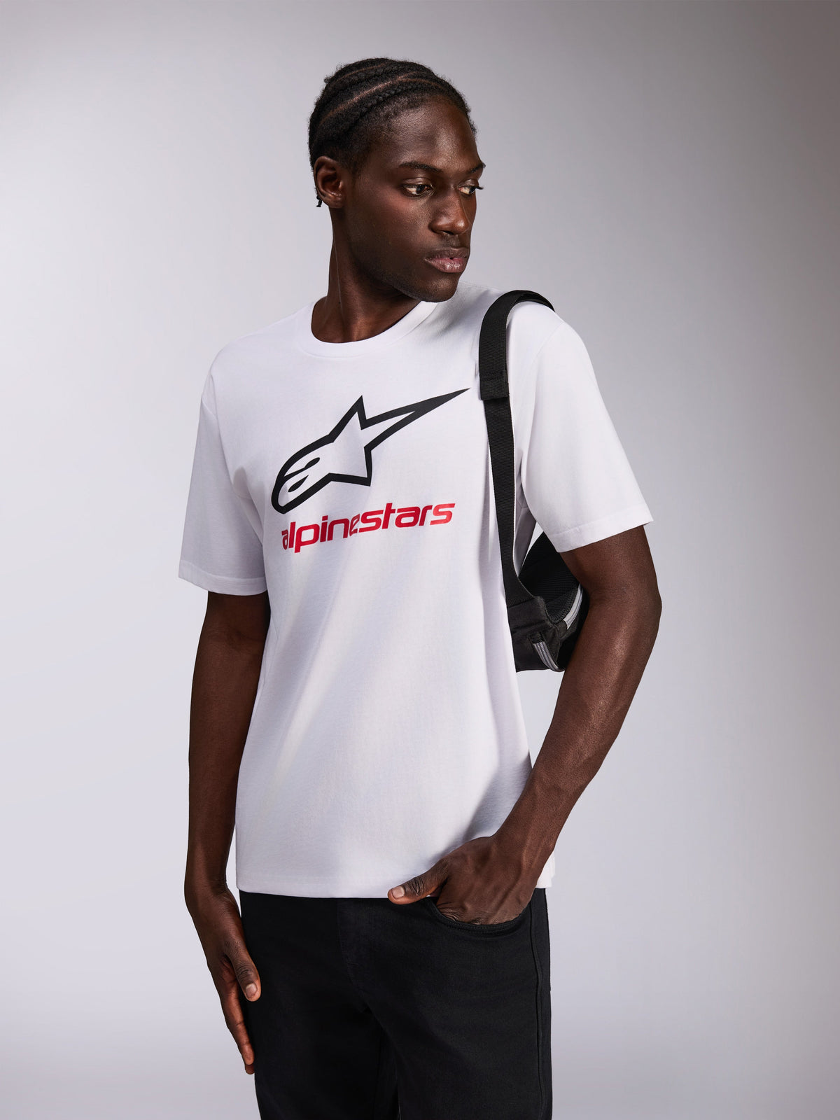 Alpinestars Always 2.0 CSF Tee, T-shirt met korte mouwen, wit, zwart sterlogo en rode Alpinestars tekst, gedragen door model met zwarte crossbodytas, casual motorsport sportkleding