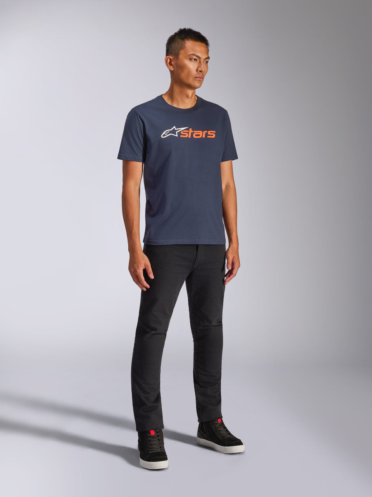 Alpinestars Blaze 2.0 CSF Tee, T-shirt met korte mouwen, marineblauw met wit en oranje Blaze-logo, gedragen door model met zwarte broek en sneakers, casual op motorsport geïnspireerde streetwear