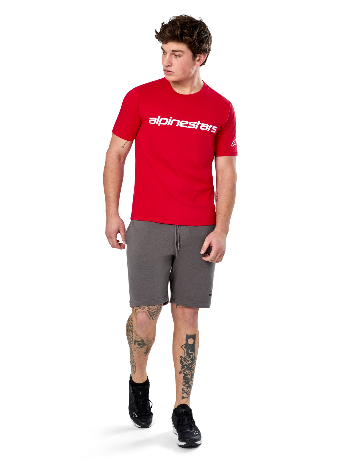 Alpinestars Linear Wordmark 2.0 CSF Tee, T-shirt met korte mouwen, rood met wit woordmerklogo op de borst, gedragen door model met grijze korte broek en zwarte sneakers, casual motorsport-geïnspireerde streetwear