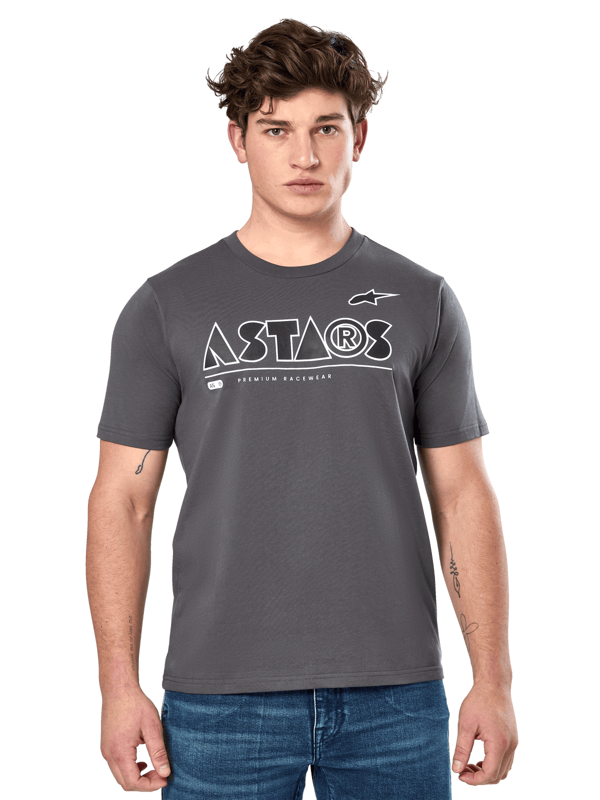 Alpinestars Cereal CSF Tee, antracietgrijs T-shirt met korte mouwen, gedragen door een mannelijk model met een blauwe jeans, wit geometrisch ASTARS-logo en 'Premium Racewear'-tekst, casual motorsport-geïnspireerde lifestyle kleding