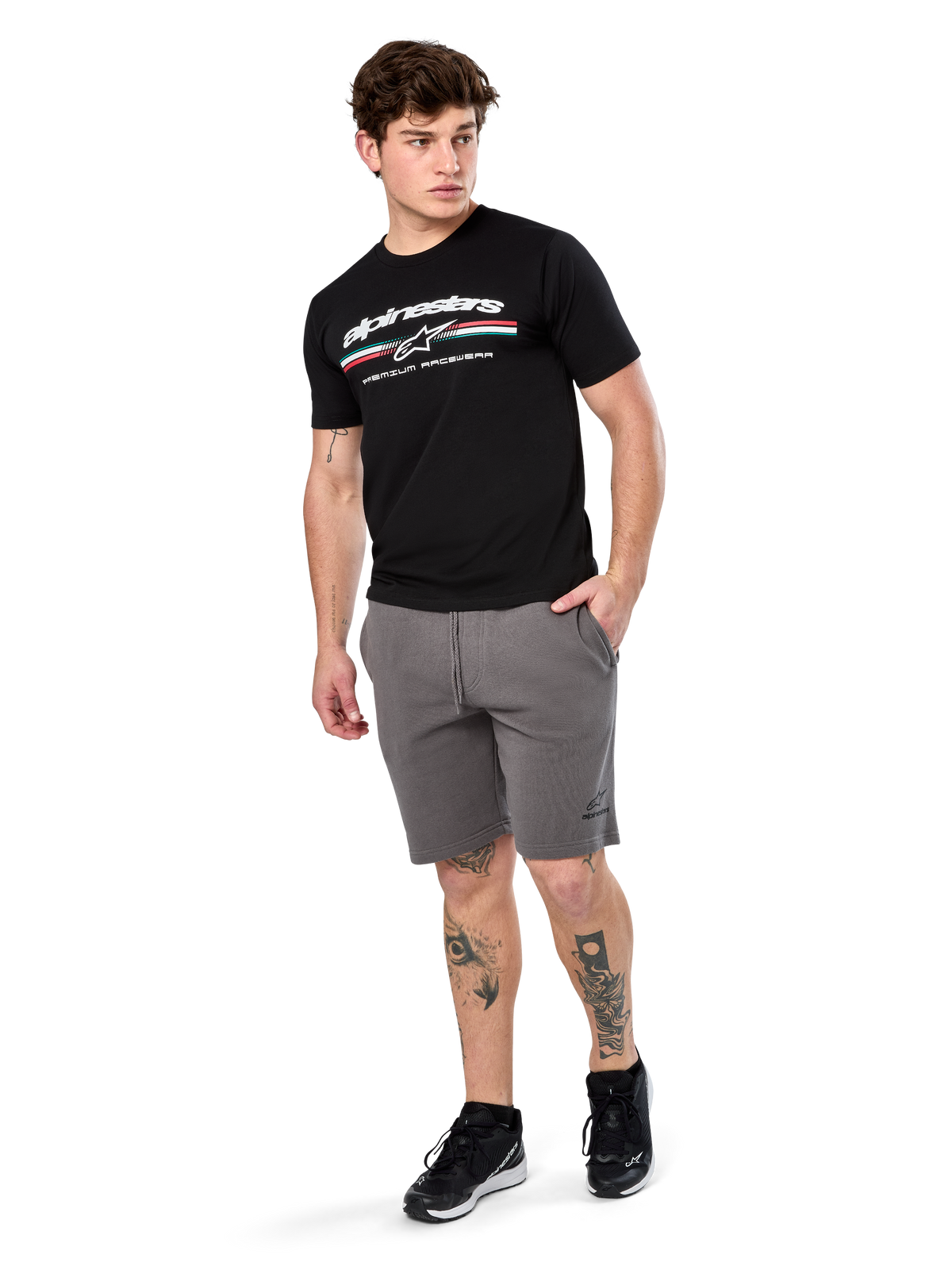 Alpinestars Prevail Csf Tee, T-shirt met korte mouwen, zwart, wit Alpinestars-logo met driekleurige paddock-streep, gedragen met grijze shorts en zwarte sneakers, casual motorsport streetwear