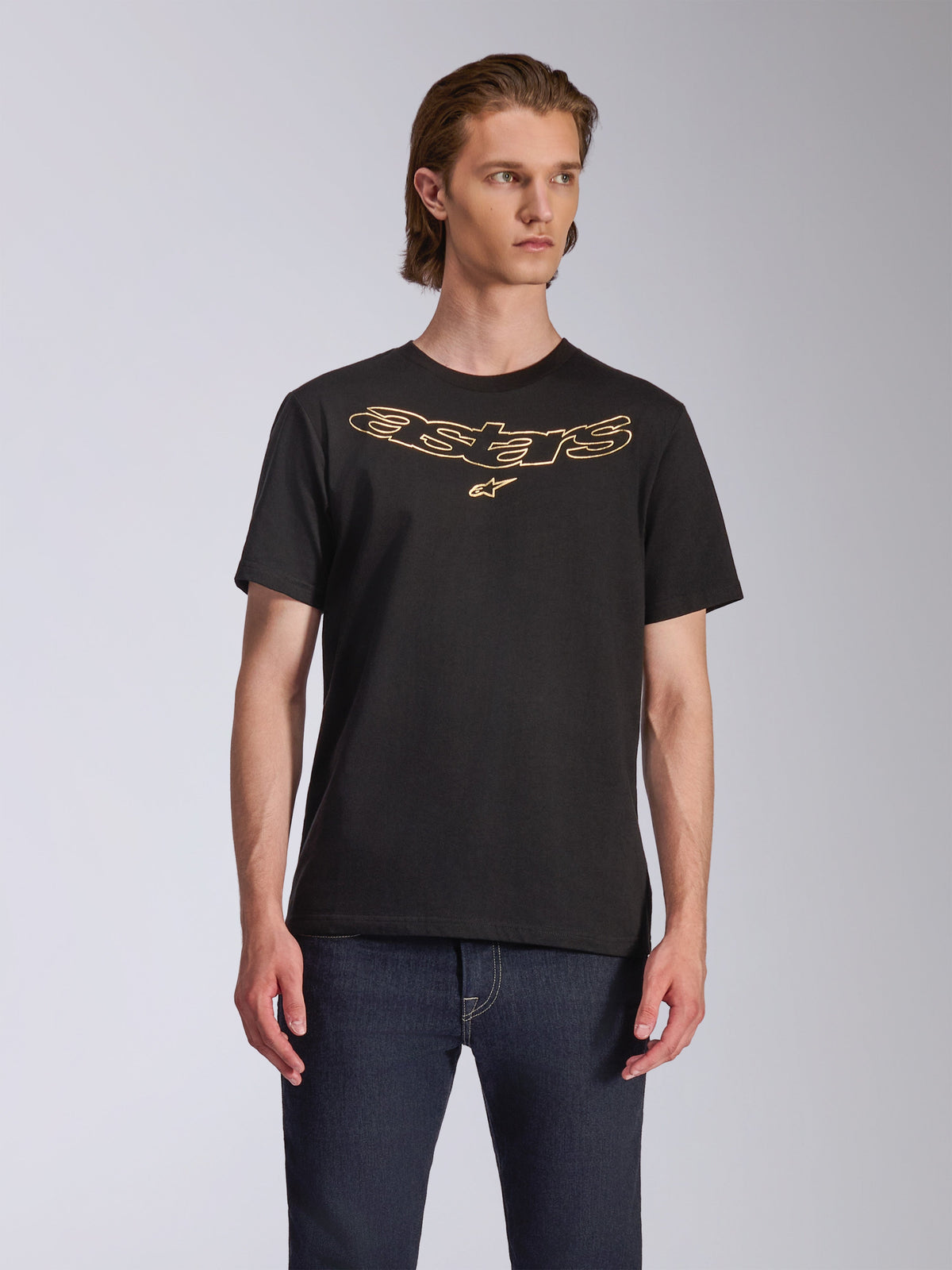 Alpinestars Luxo CSF Tee, T-shirt met korte mouwen, zwart, goud omlijnd Astars-logo op de borst, gedragen met donkerblauwe jeans, casual motorsport streetwear