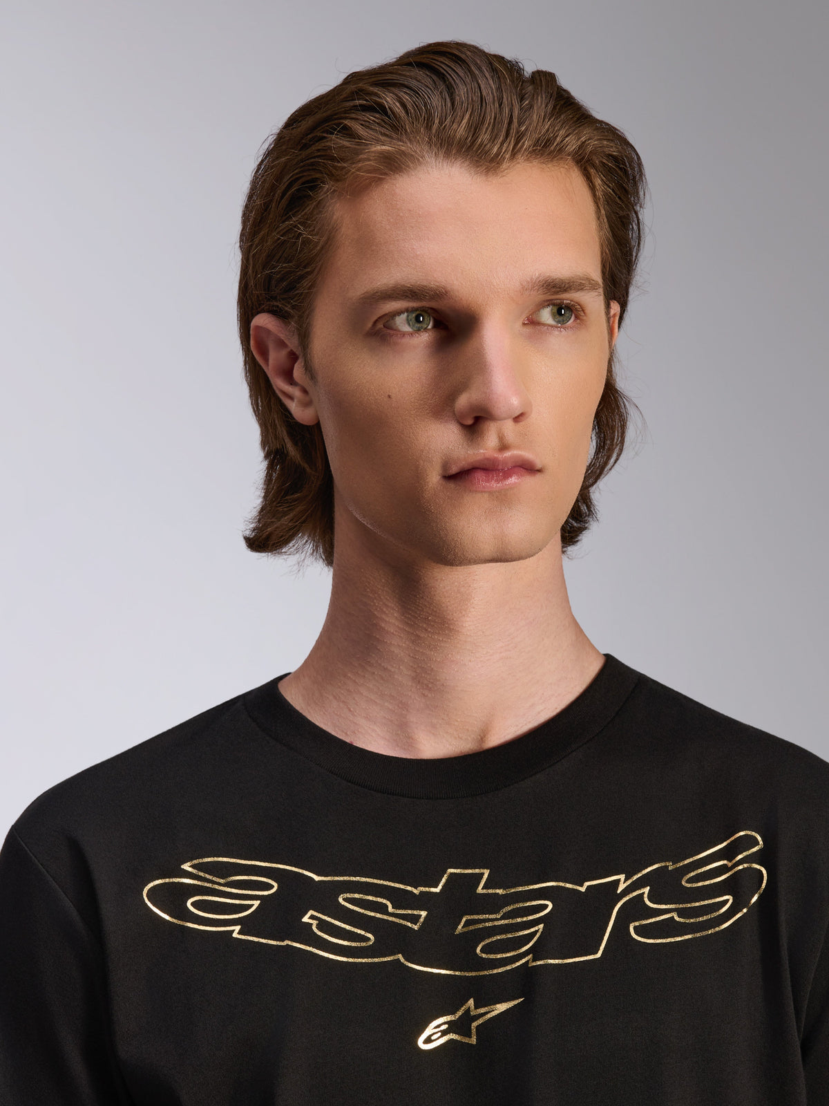 Alpinestars Luxo CSF Tee, T-shirt met korte mouwen, zwart met goud metallic Astars-logo op de borst, gedragen door een mannelijk model, casual motorsport-geïnspireerd ontwerp