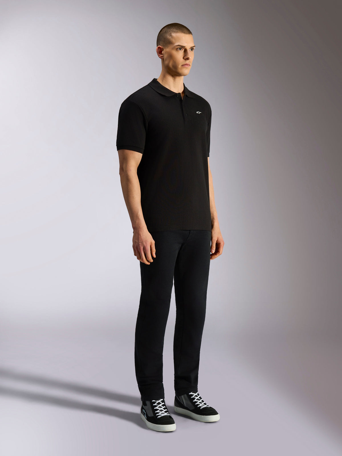 Alpinestars Endeavor Classic Polo, black short sleeve polo shirt, pique knit with three-button placket, small white Astars logo on the left chest, worn with black pants and sneakers, casual motorsport streetwear
