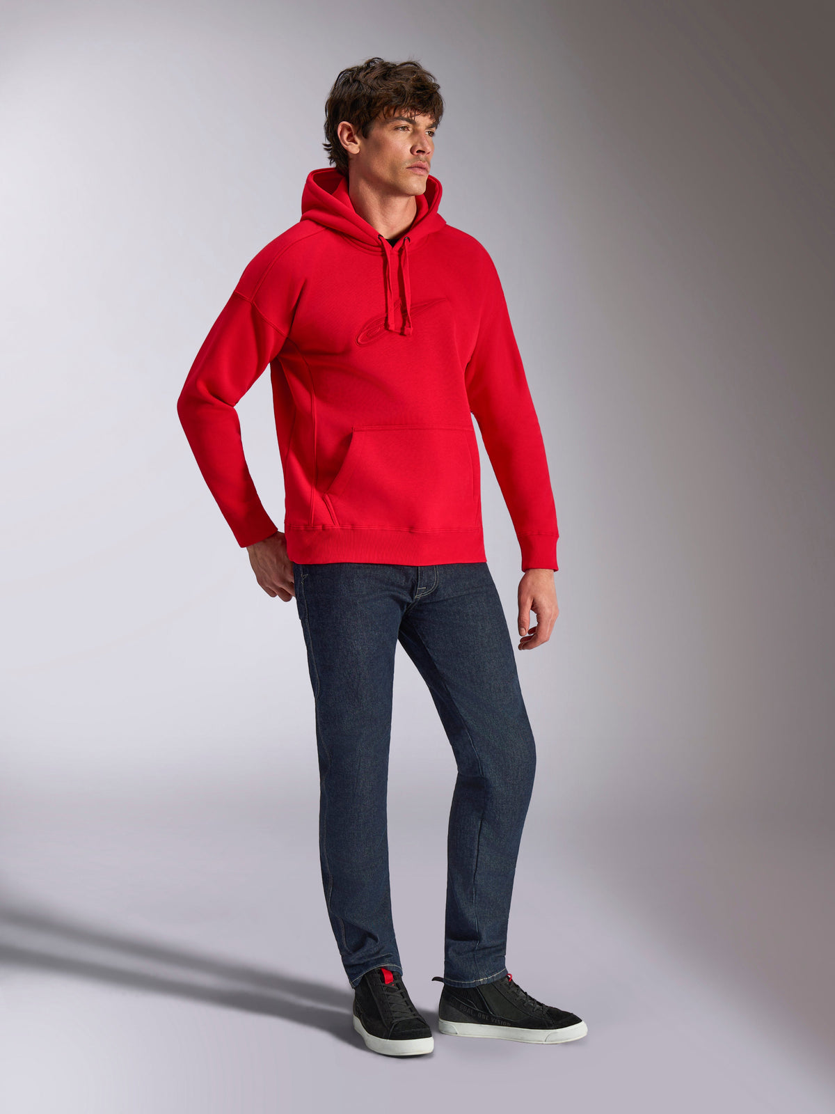 Alpinestars Emergent Oversized Hoodie, rood, pullover fleece hoodie met ton-sur-ton 3D-geborduurd logo, oversized pasvorm, gedragen door een model met een donkerblauwe jeans en zwarte sneakers, casual op motorsport geïnspireerde streetwear