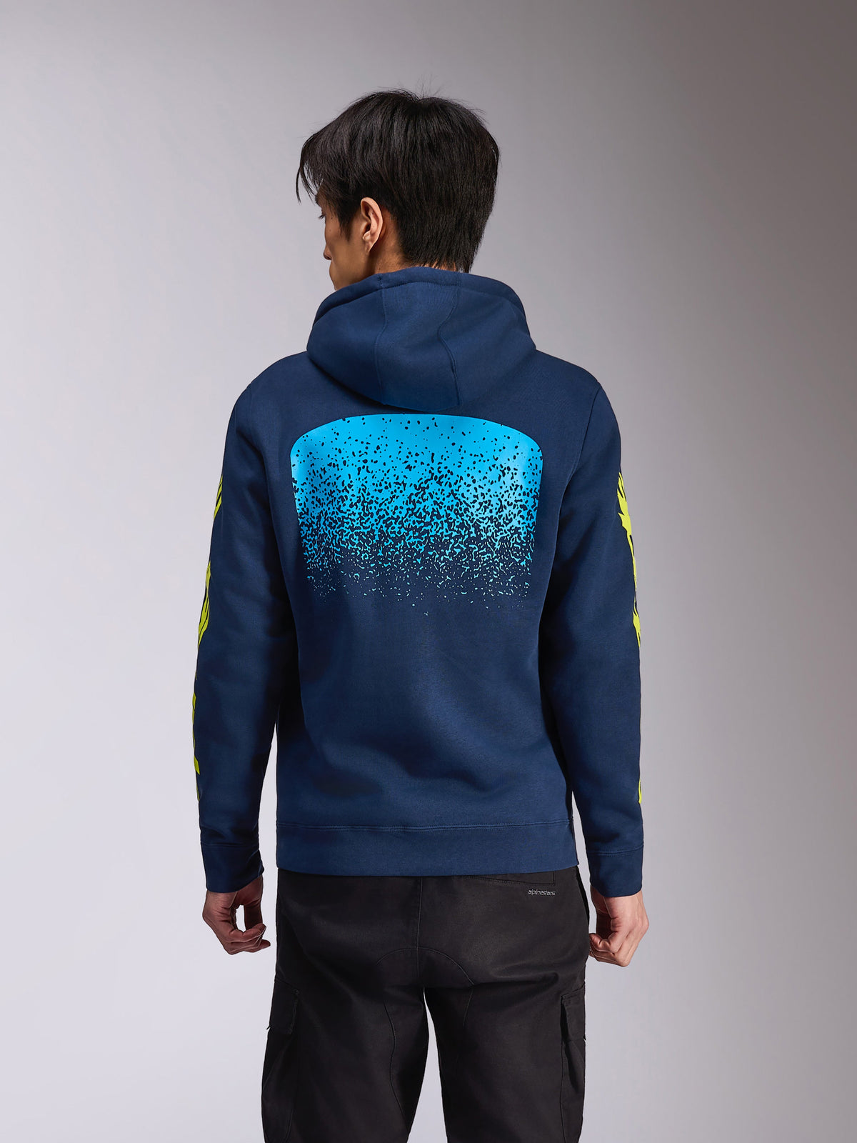 Alpinestars Obsessed Hoodie, donkerblauwe fleece hoodie met capuchon, achteraanzicht met een grote lichtblauwe MX-verloopgraphic, gele Alpinestars woordlogo's op de mouwen, casual motorsport-geïnspireerde streetwear