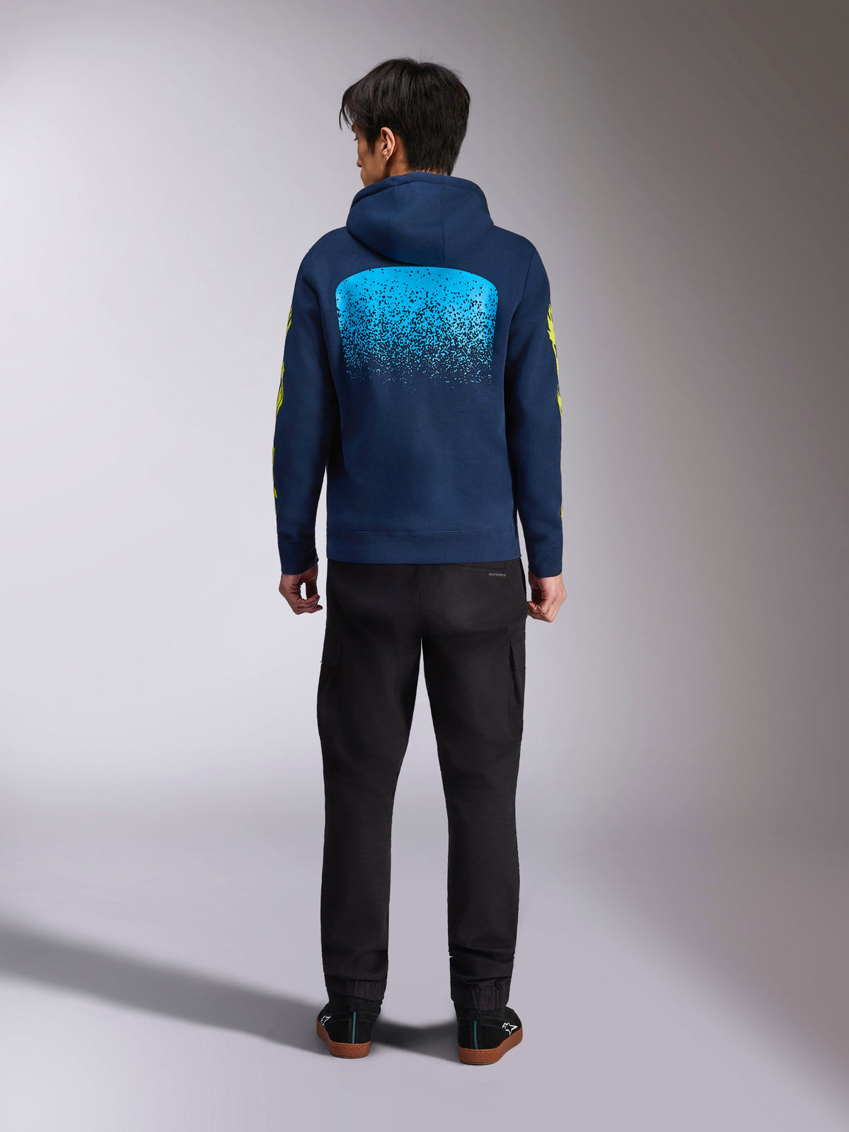 Alpinestars Obsessed Hoodie in Navy blauw, achteraanzicht met een grote cyaan MX-verloopgraphic en gele logo's op de mouwen, casual motorsport-geïnspireerde pullover fleece.