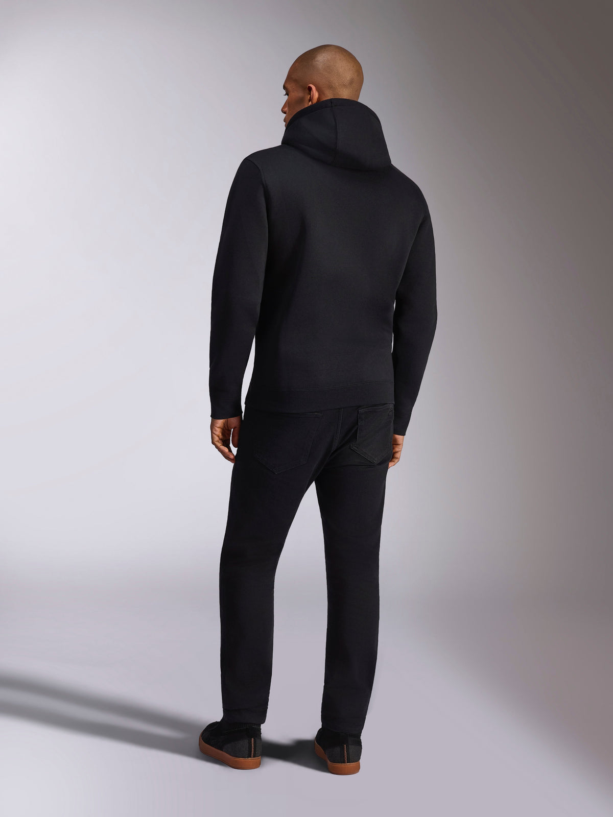 Alpinestars Ellipsoid Hoodie, casual sportkleding, effen zwarte fleece pullover met capuchon, achteraanzicht, voorzien van lange mouwen en een geribde zoom, gecombineerd met een zwarte broek, modern op motorsport geïnspireerd ontwerp