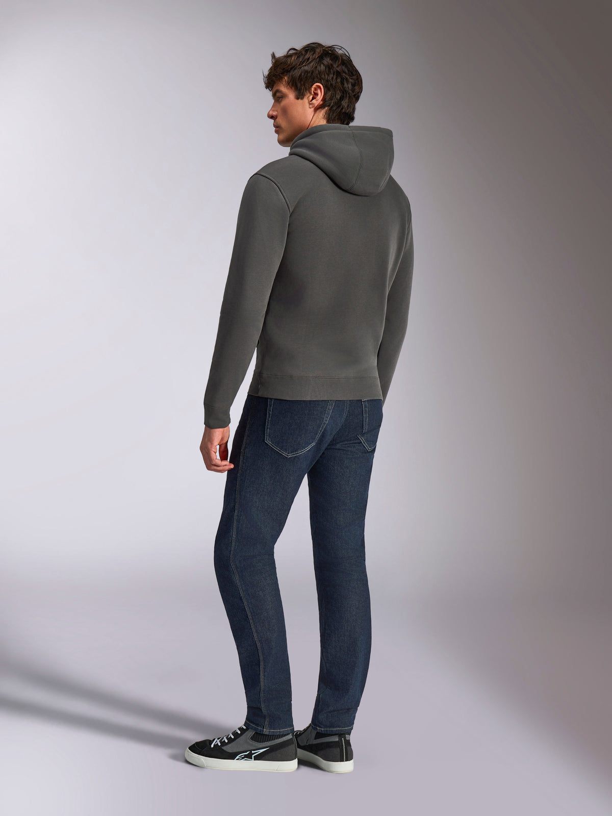Alpinestars Ellipsoid Hoodie, casual sportkleding, gunmetal grijs, achteraanzicht op mannelijk model, capuchon met trekkoord, lange mouwen, geribde manchetten en zoom, gecombineerd met donkere jeans en sneakers