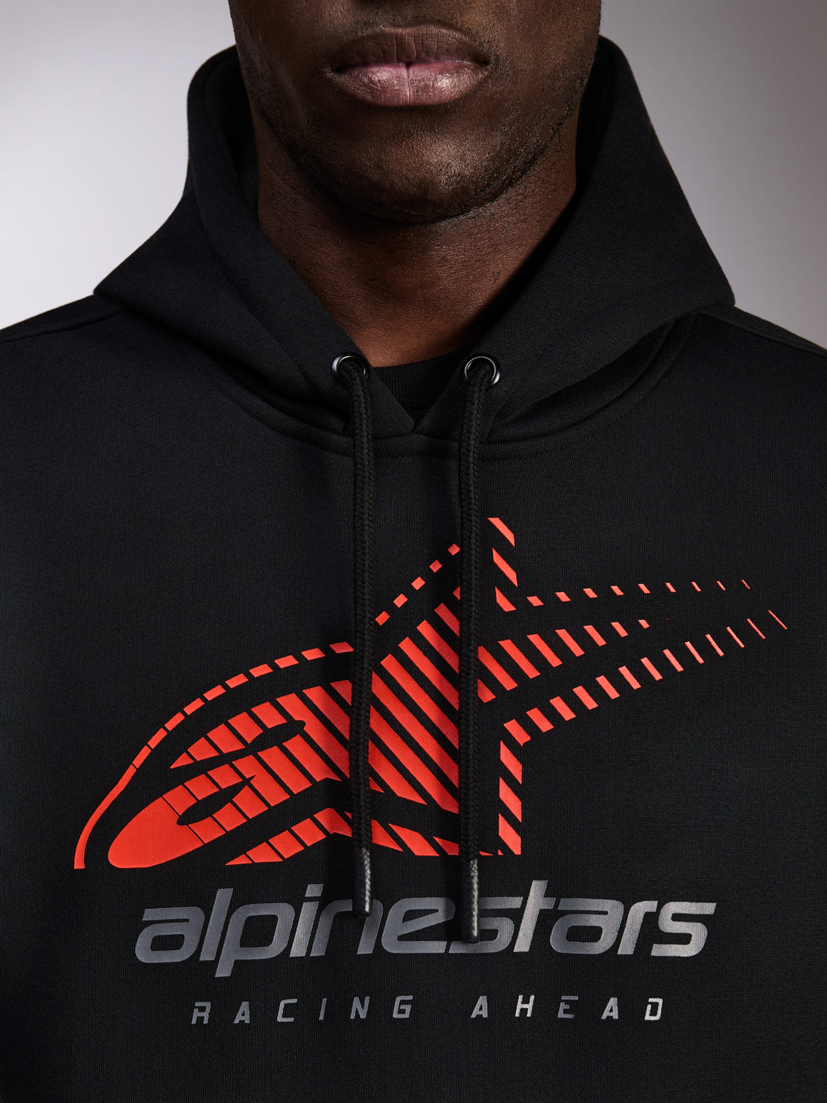 Alpinestars Pulse Hoodie, black pullover hoodie, close-up of chest featuring red Astars logo with speed line fade and silver branding, black drawstrings with dipped tips, casual motorsport streetwear
