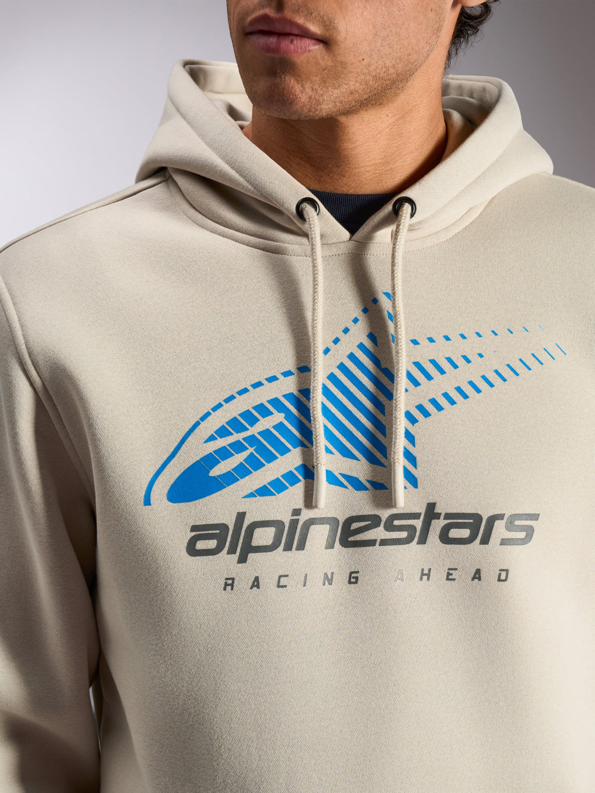 Alpinestars Pulse Hoodie, Off White casual streetwear pullover, close-up van de borst met blauw en grijs Astars Combo Logo met speed line fade en 'Racing Ahead'-tekst, capuchon met trekkoord en gedipte uiteinden.