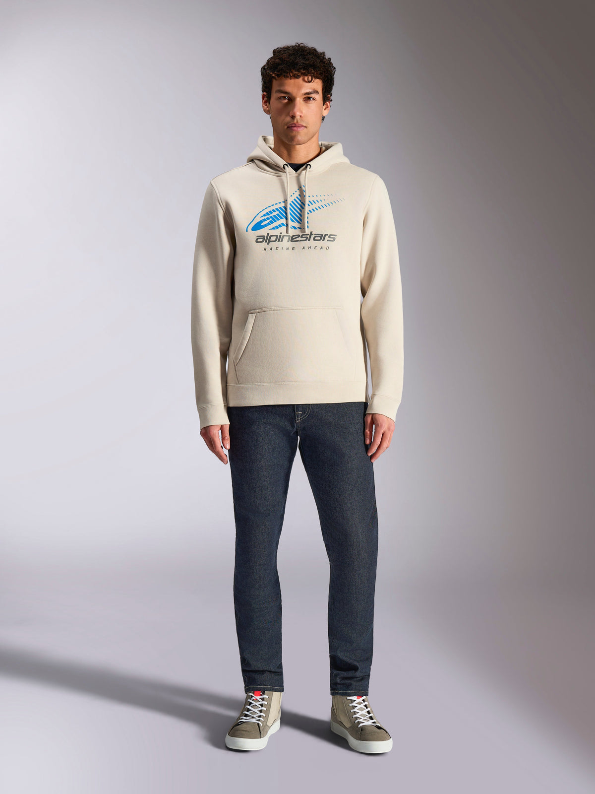 Alpinestars Pulse Hoodie, Off White, pullover met lange mouwen en capuchon met trekkoord, blauw en zwart Astars Combo Logo met speed line fade, gecombineerd met een donkere jeans en sneakers, casual motorsport streetwear
