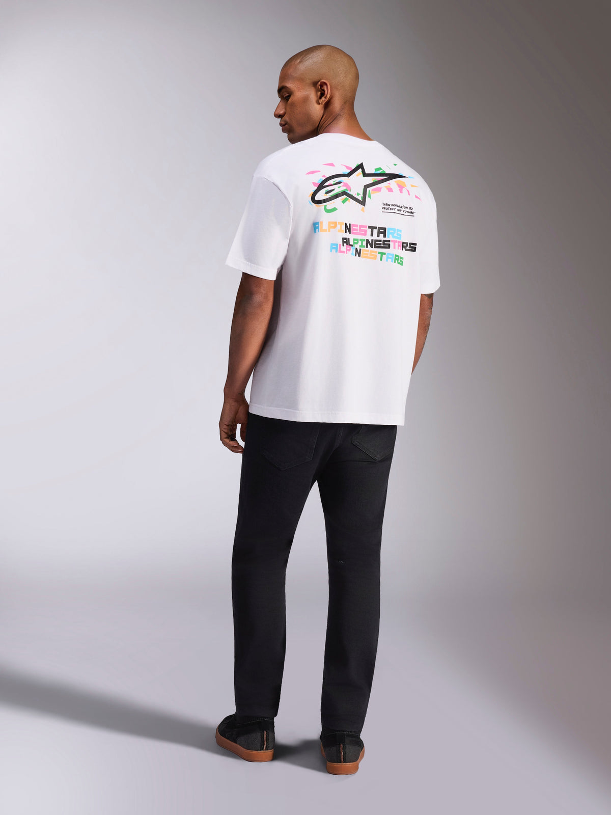 Alpinestars Wild Oversized CSF Tee, T-shirt met korte mouwen, wit, achteraanzicht van model in oversized shirt met levendig meerkleurig Astars-logo en gestapelde tekst op de rug, casual op motorsport geïnspireerde streetwear