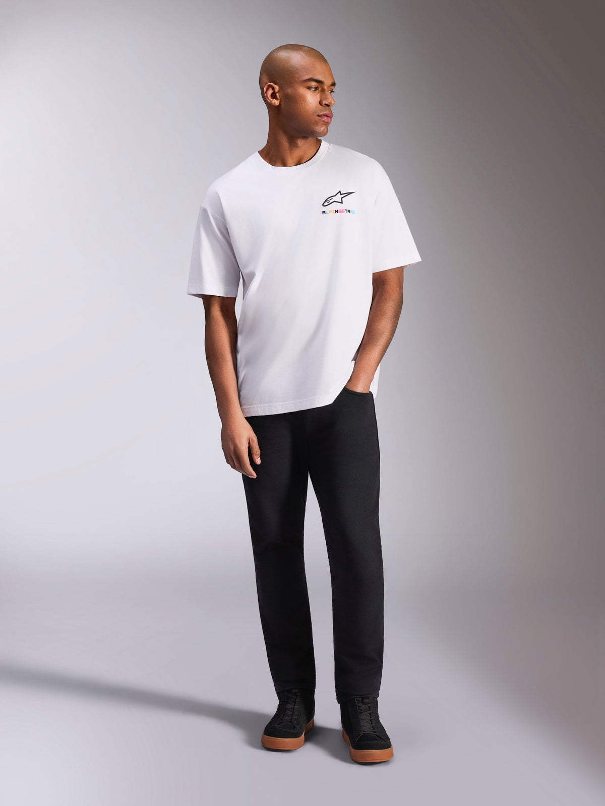 Alpinestars Wild Oversized CSF Tee, T-shirt met korte mouwen, wit, levendig meerkleurig Astars-logo op de borst, gedragen met een zwarte broek en sneakers, casual motorsport lifestyle-kleding