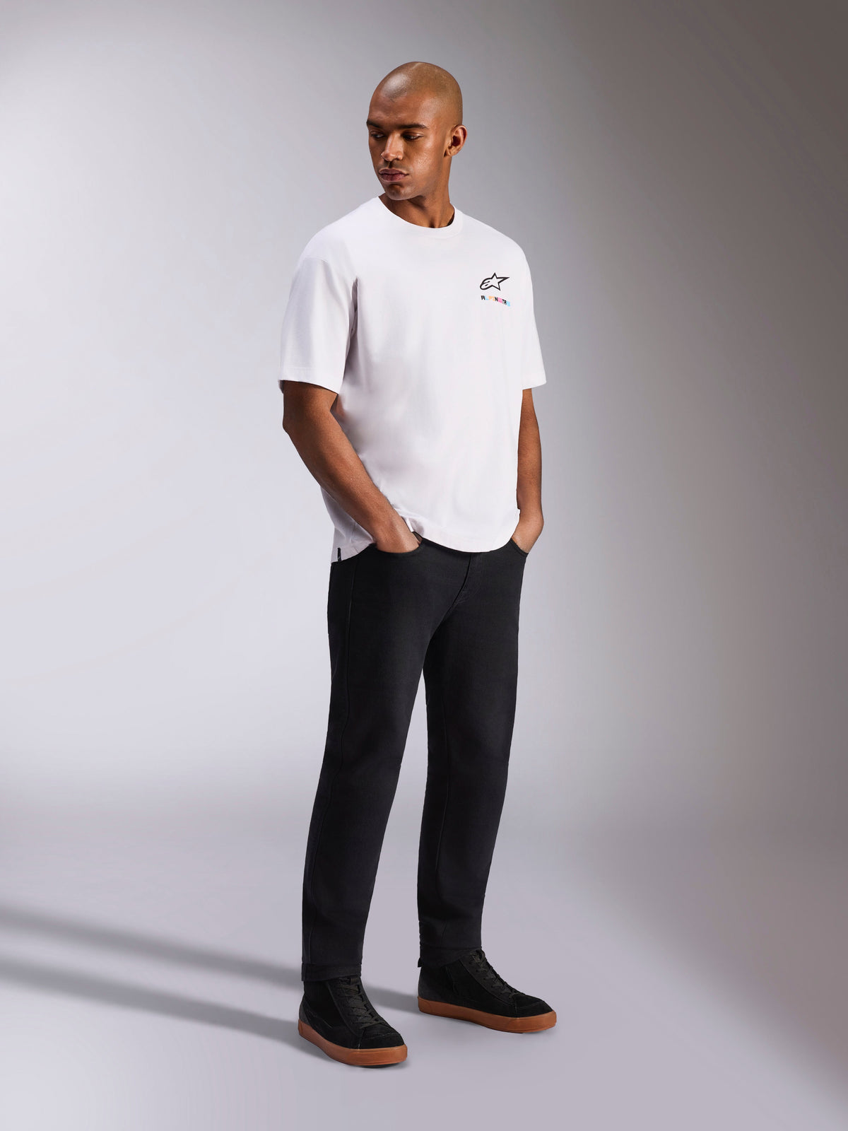 Alpinestars Wild Oversized CSF Tee, T-shirt met korte mouwen, wit, met een klein meerkleurig Astars-logo op de borst, gedragen door een model met een zwarte broek en zwarte sneakers, casual motorsport-geïnspireerde streetwear