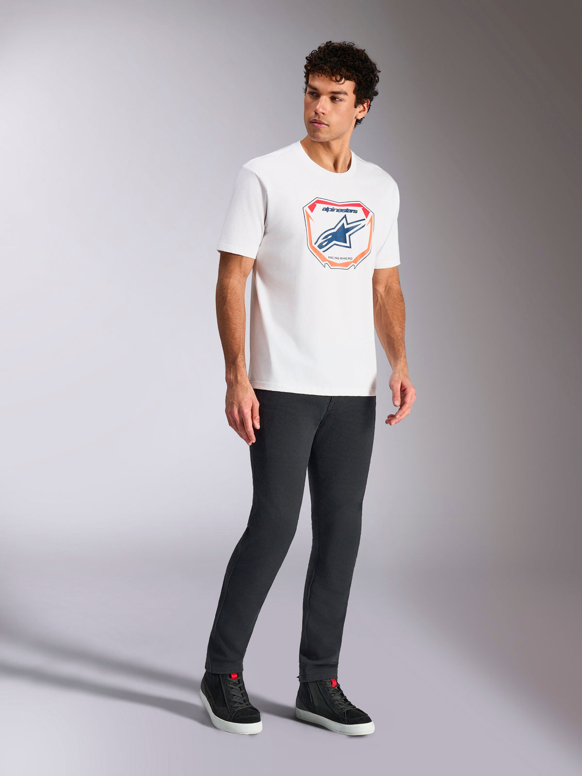 Alpinestars Plate CSF Tee, T-shirt met korte mouwen, wit, voorzien van een Astars MX plaatgrafiek aan de voorzijde in blauw en oranje, casual op motorsport geïnspireerde streetwear gedragen met een donkere broek en hoge sneakers