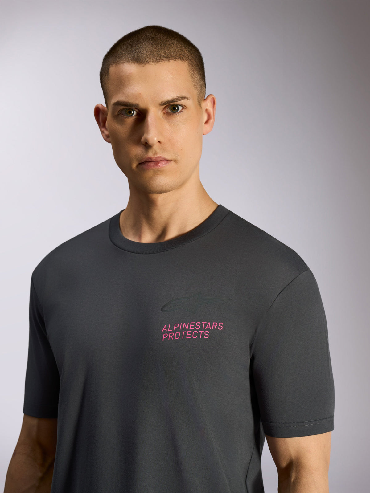Alpinestars Pop Helmet CSF Tee, Short Sleeve T-Shirt, Charcoal Gray, worn by model, featuring pink 'ALPINESTARS PROTECTS' text and Astars logo on chest, casual motorsport streetwear