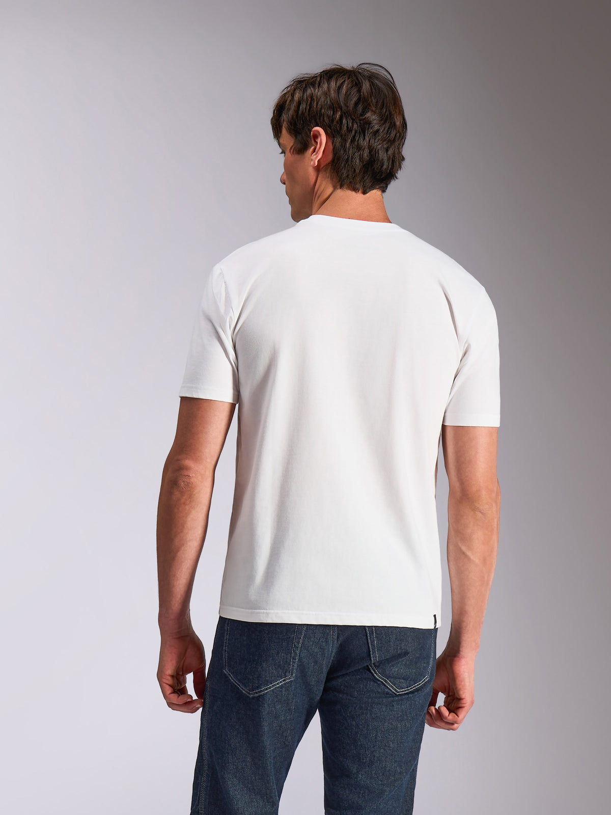 Alpinestars Abus CSF Tee, T-shirt met korte mouwen, wit, achteraanzicht van model in effen wit T-shirt en donkerblauwe jeans, casual op de motorsport geïnspireerde lifestyle-kleding