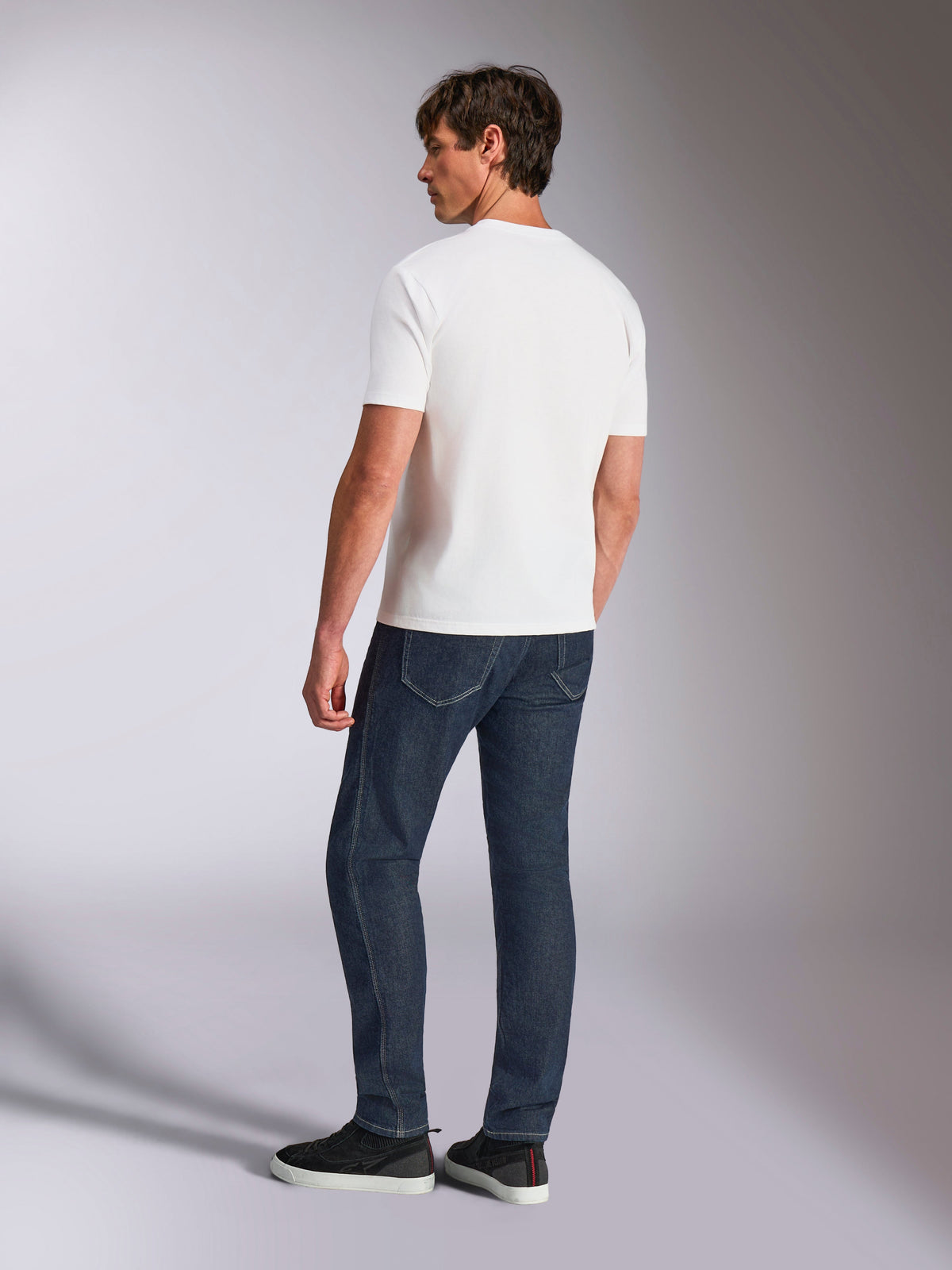 Alpinestars Abus CSF Tee, T-shirt met korte mouwen, wit, achteraanzicht op model die een donkerblauwe jeans en zwarte sneakers draagt, casual motorsport-geïnspireerd ontwerp