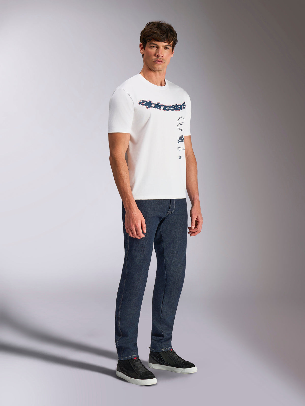 Alpinestars Abus CSF Tee, T-shirt met korte mouwen, wit, meervoudig gestapeld gebogen Alpinestars logo-ontwerp, gedragen door mannelijk model met donkerblauwe jeans en zwarte sneakers, casual motorsport streetwear