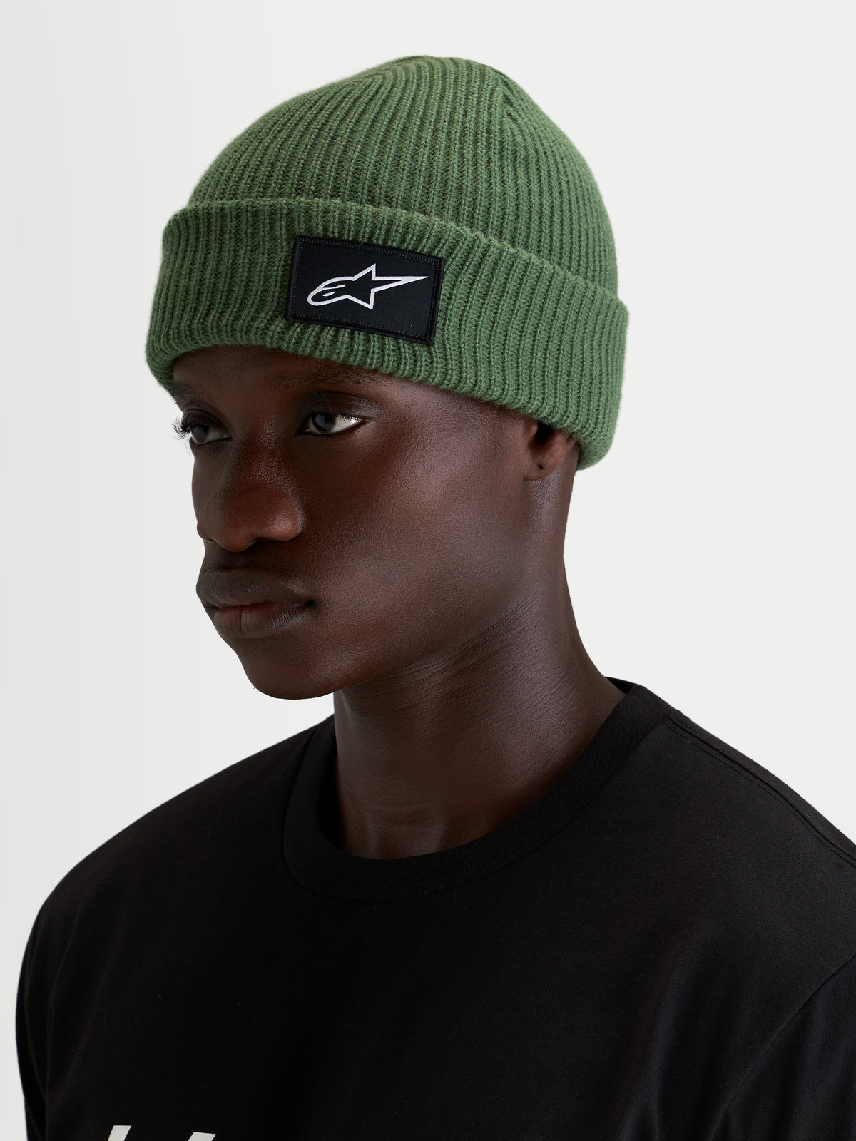 Alpinestars Unload Rib Cuff muts, erwtgroene casual wintermuts gedragen door een model, met een gebreide jerseysteek en een zwart-witte SAstars geweven patch aan de voorkant