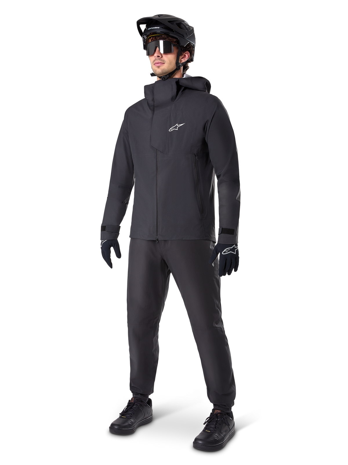 Alpinestars A-Dura Elite Waterproof Jacket in Black, worn by a male rider with matching black MTB pants, gloves, and helmet. The jacket features a technical waterproof design with a white Astars logo on the chest and a high protective collar.