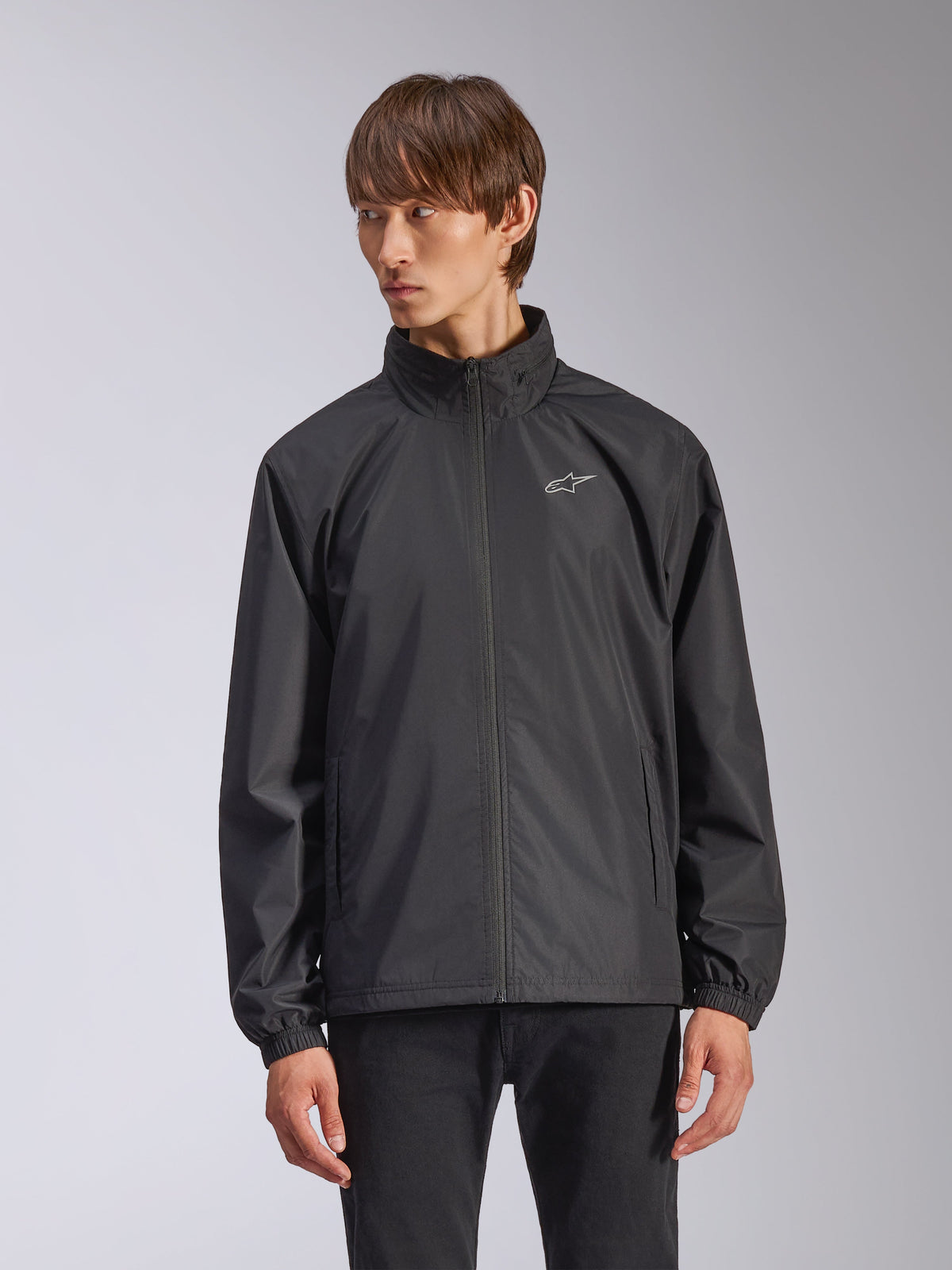 Alpinestars Overhaul Racer Jacket, zwarte regenjas voor heren, met een hoge kraag en een volledige ritssluiting aan de voorzijde, klein wit logo op de borst, elastische manchetten, gladde waterbestendige stof, minimalistisch design geïnspireerd op de motorsport
