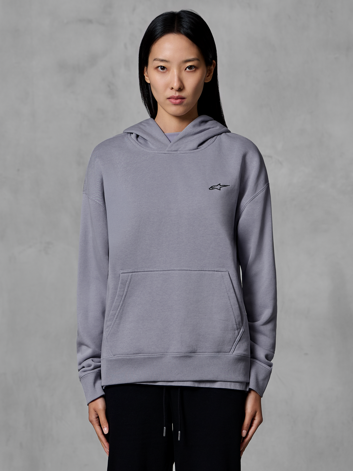 Alpinestars Essentials Ageless Hoodie, casual sportkleding, zilver met klein zwart logo, kangoeroezak, pullover met capuchon, gedragen door model, moderne lifestyle-kleding