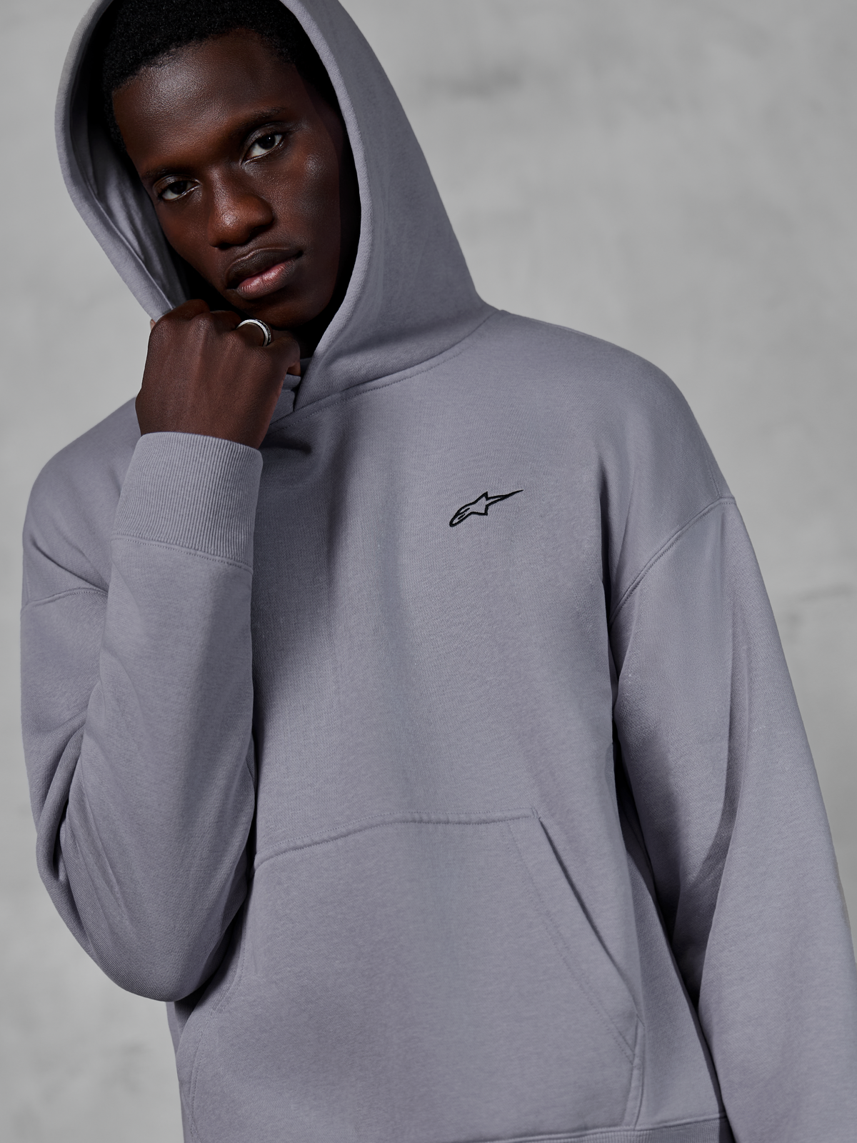 Alpinestars Essentials Ageless Hoodie, zilver, mannelijk model draagt de hoodie met de capuchon op, klein zwart Alpinestars-logo op de borst, kangoeroezak, geribbelde boorden, casual lifestyle streetwear