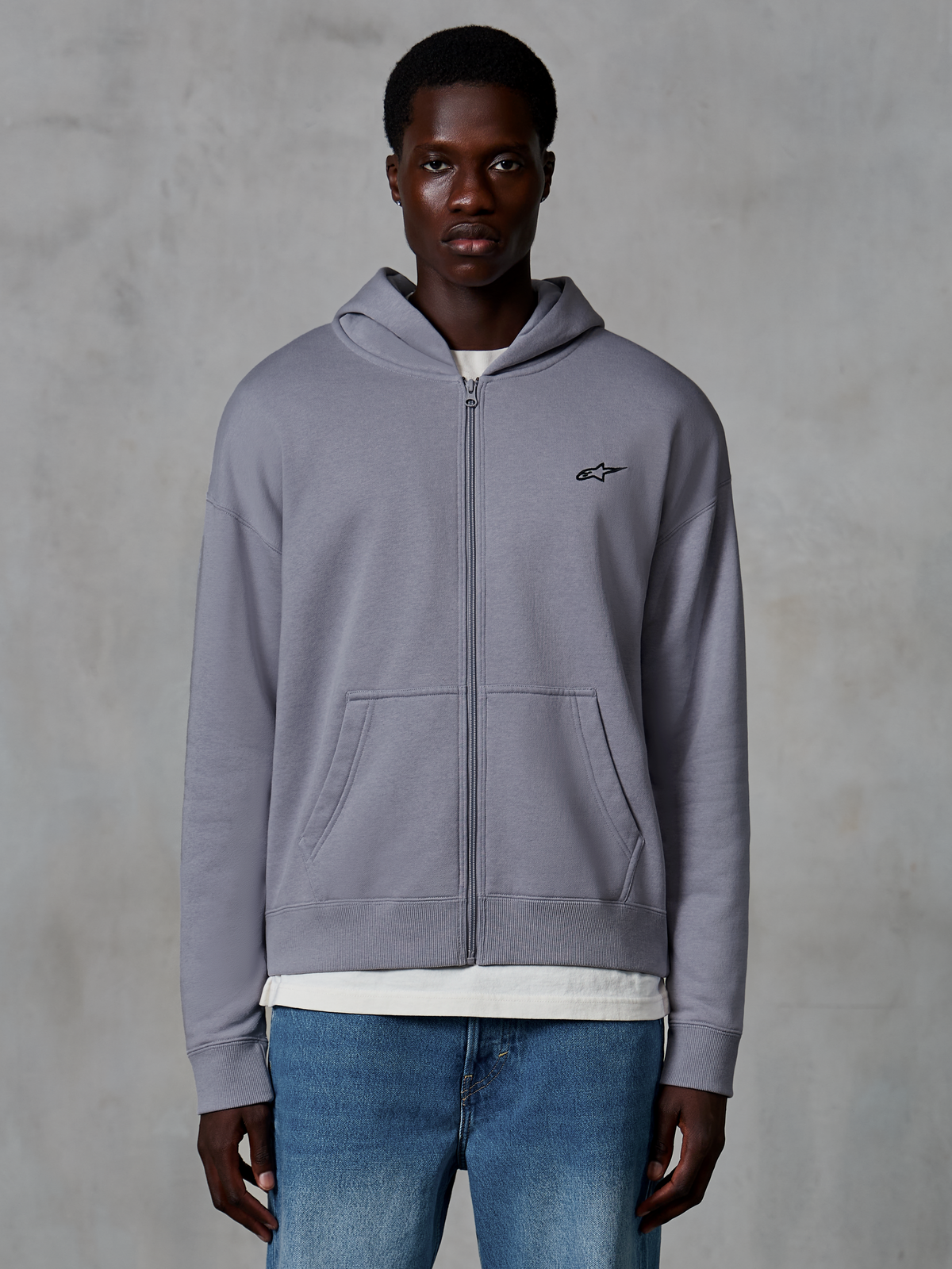 Alpinestars Essentials Ageless Zip Hoodie, zilver, casual streetwear gedragen door model, fleece met volledige ritssluiting en klein zwart Astars-logo op de borst, kangoeroezakken, ontspannen pasvorm