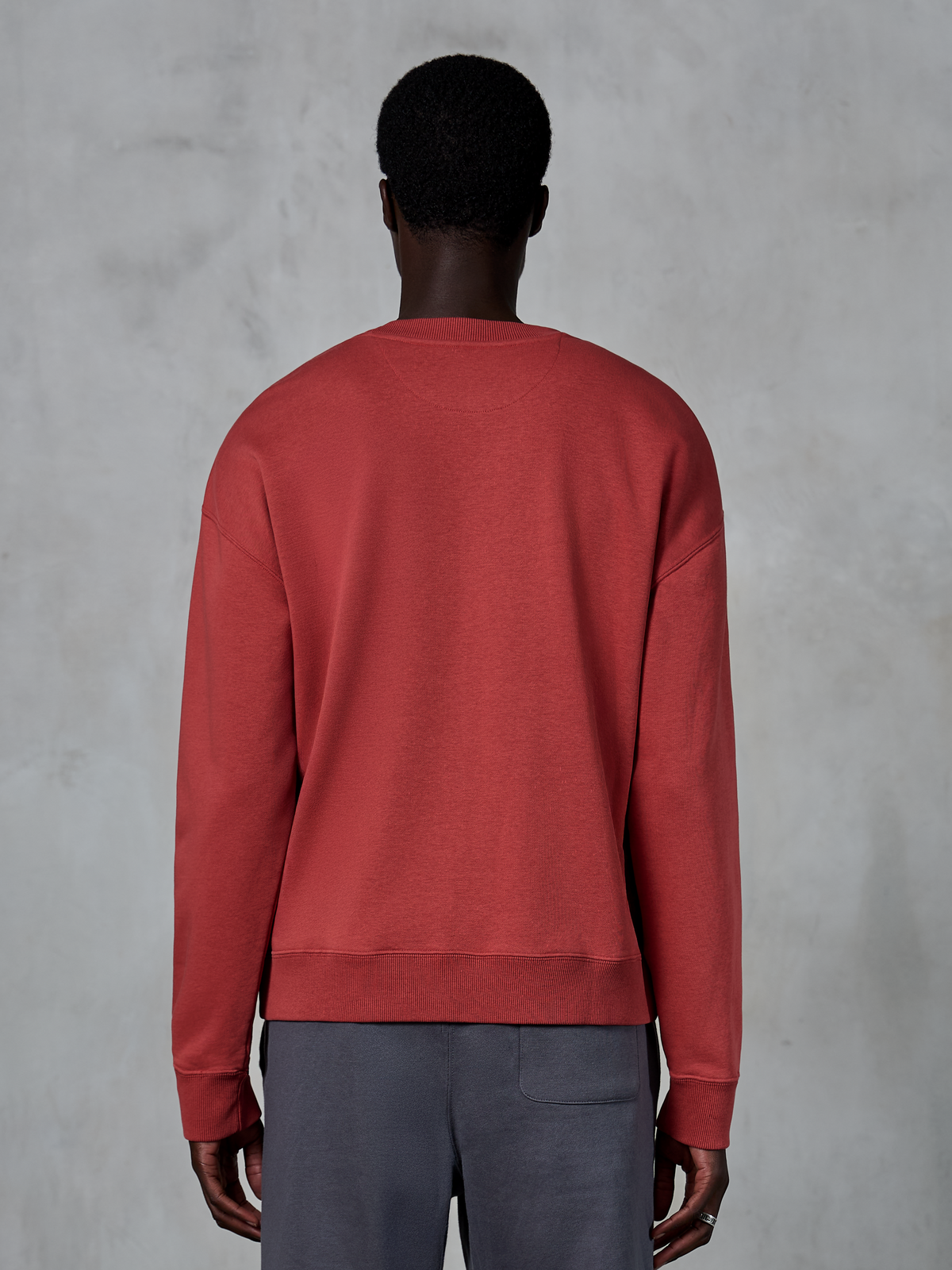 Alpinestars Essentials Ageless Crew, Brick Red sweatshirt met ronde hals, achteraanzicht van model dat een relaxed fit pullover draagt, geribbelde kraag en boorden, casual op de motorsport geïnspireerde streetwear