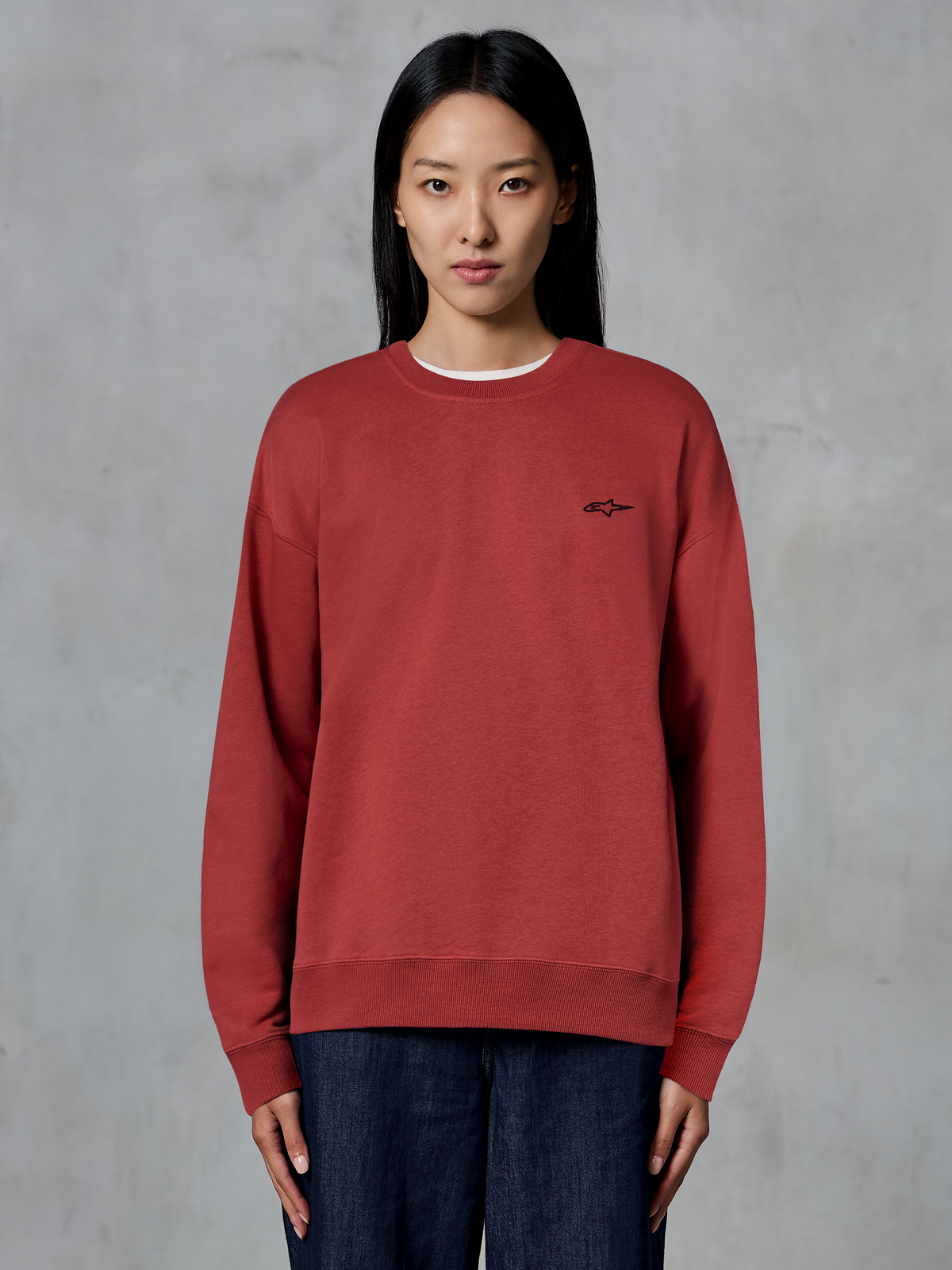Alpinestars Essentials Ageless Crew, baksteenrode crewneck sweatshirt, klein zwart logo op de borst, premium fleece, gedragen door model, casual op motorsport geïnspireerde streetwear