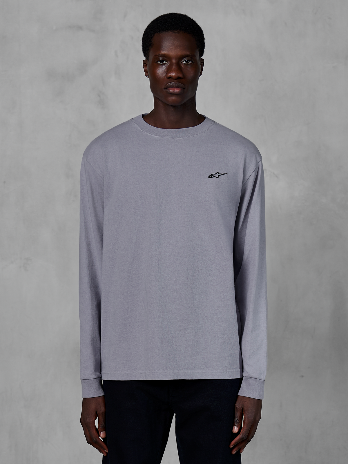 Alpinestars Essentials Ageless LS Tee, T-shirt met lange mouwen, zilver, gedragen door een model, met een klein zwart Alpinestars-logo op de borst, ontspannen eigentijdse pasvorm, biologisch katoen, casual streetwear