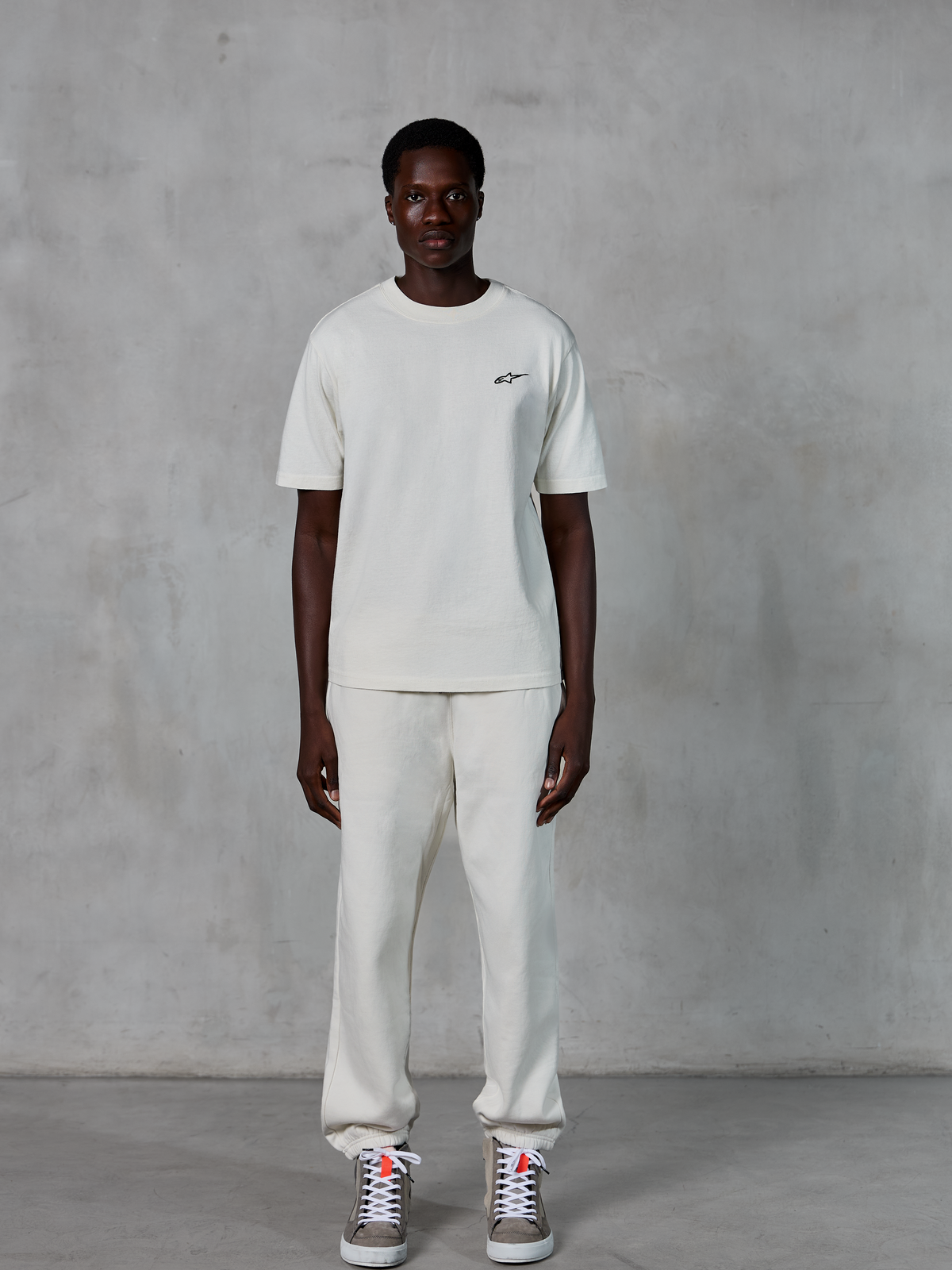 Alpinestars Essentials Ageless SS Tee, Short Sleeve T-Shirt, Off White, featuring a small black Alpinestars logo on the chest, styled with matching joggers and sneakers for a relaxed lifestyle look