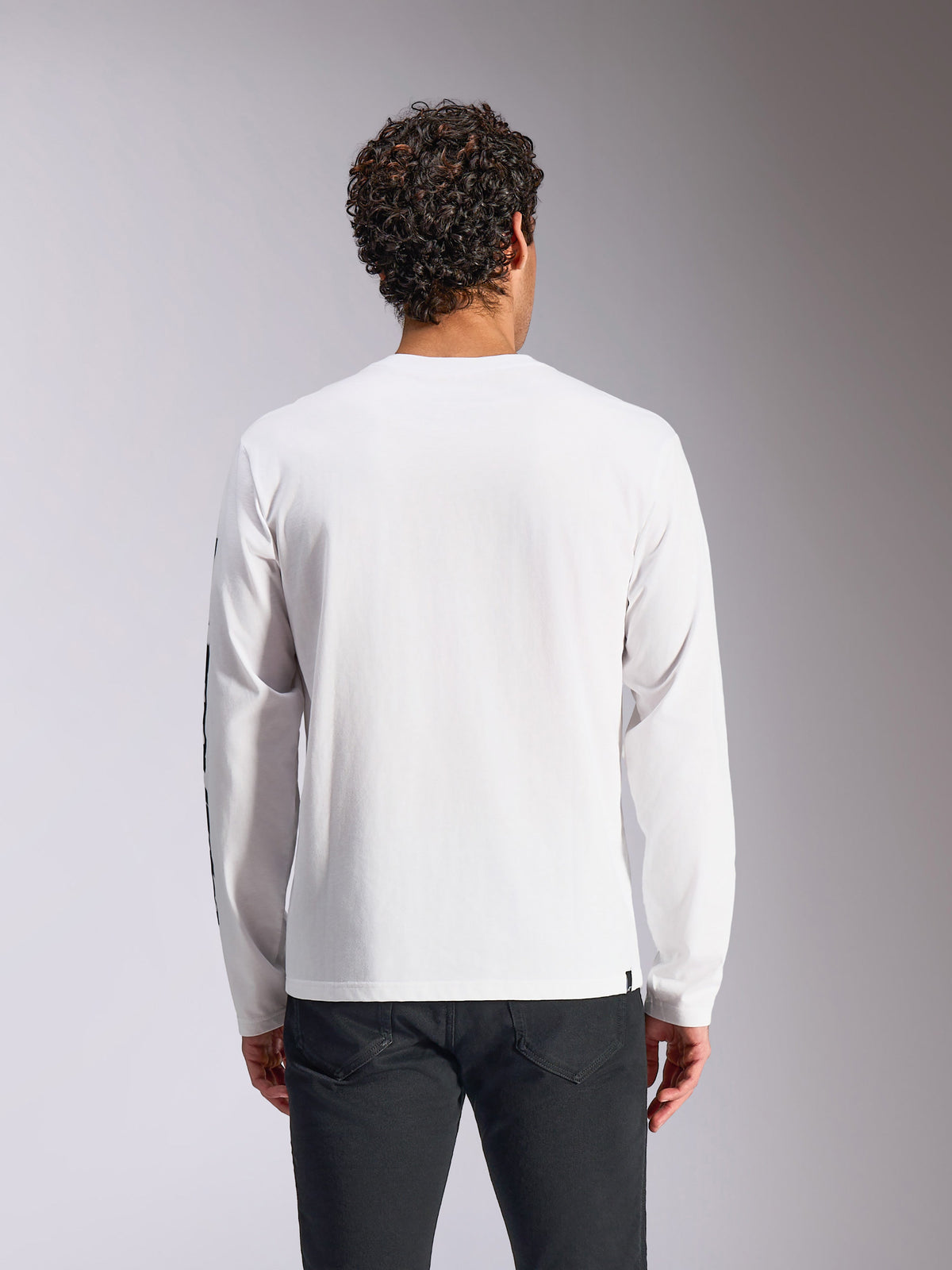 Alpinestars Trackside CSF Tee - Lange Mouwen, wit, achteraanzicht op model, gecombineerd met een zwarte broek, witte stof met lange mouwen, casual streetwear geïnspireerd op de motorsport