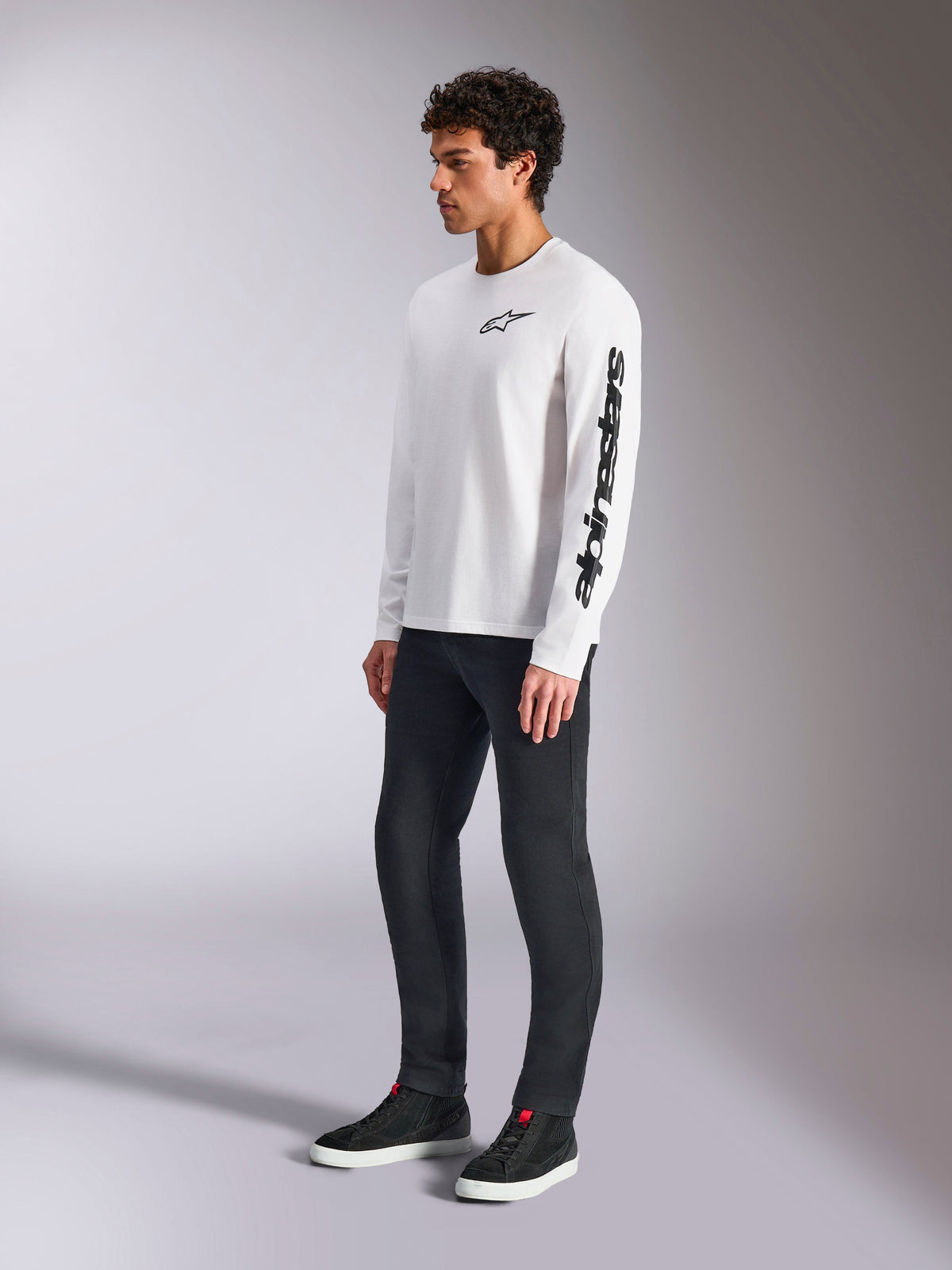 Alpinestars Trackside CSF Tee, T-shirt met lange mouwen, wit, zwart sterlogo op de borst en woordmerk op de linkermouw, gedragen door een mannelijk model met donkere broek en sneakers, casual lifestyle sportkleding