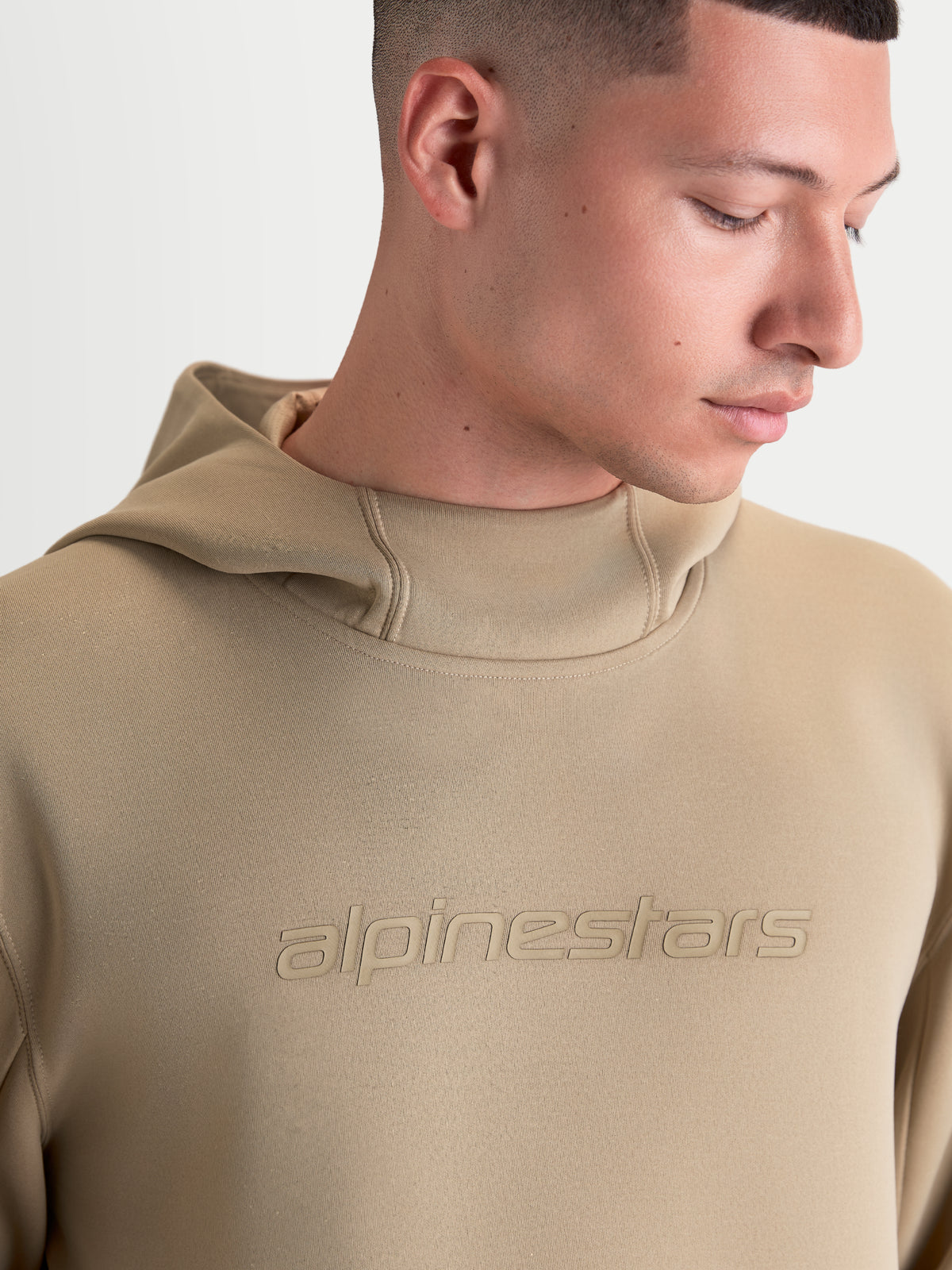 Alpinestars Datrix hoodie, sportswearpullover voor heren en dames, bruin, voorzien van een tonaal Alpinestars-logo en capuchon met meshvoering, close-up van een model die de premium fleececonstructie toont.