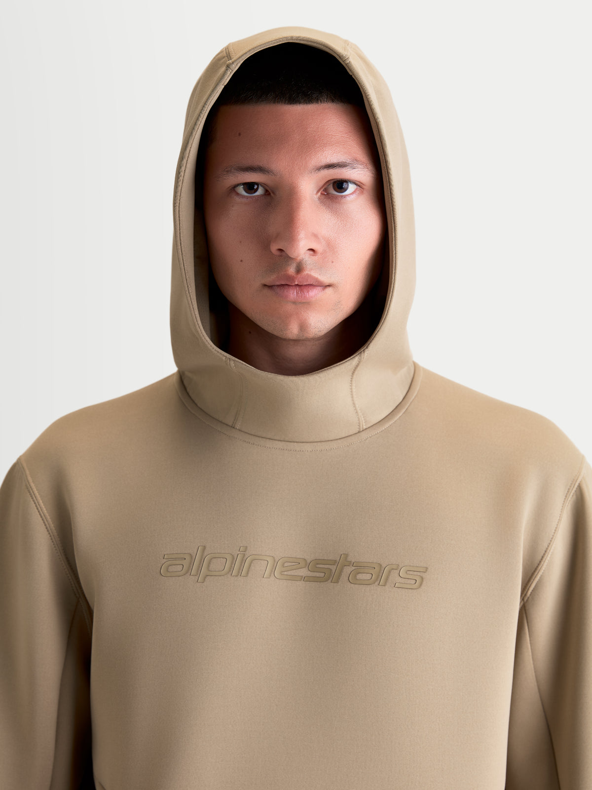Alpinestars Datrix Hoodie, casual sportswear pullover voor heren en dames, bruin, vooraanzicht close-up op model met capuchon op, voorzien van tonale Alpinestars-branding en premium tri-blend fleece materiaal.