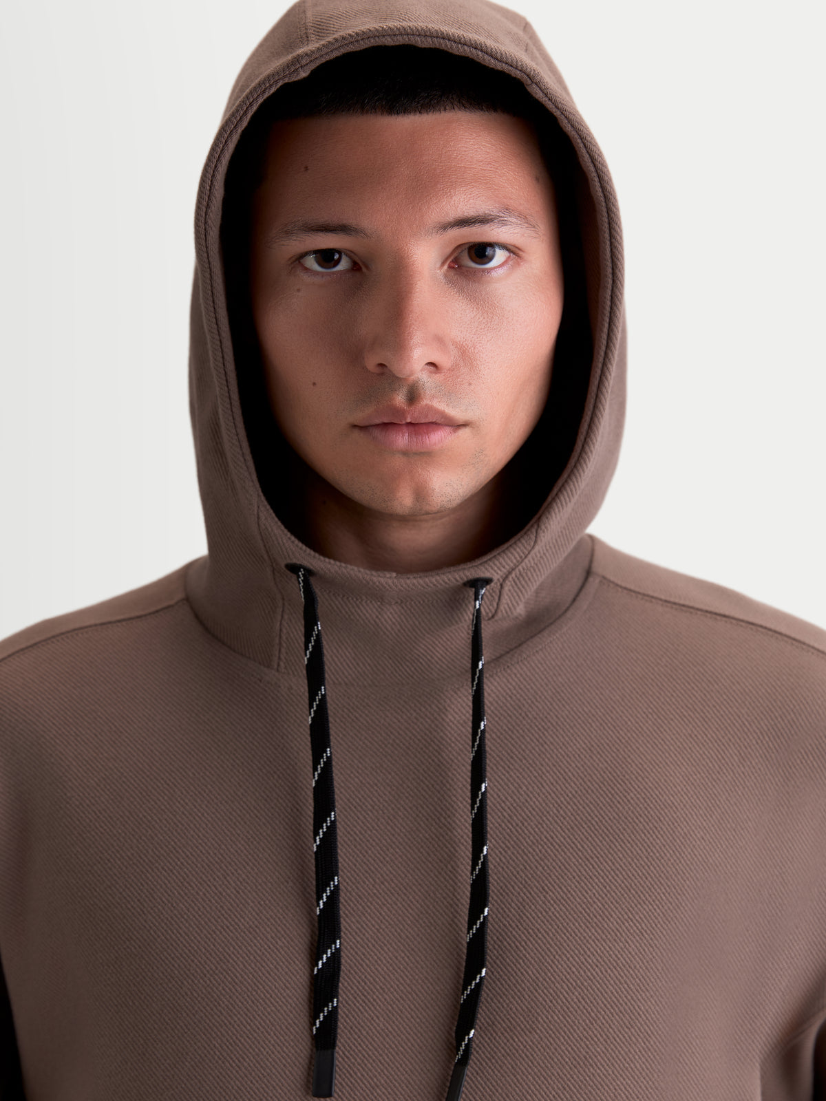 Alpinestars Camino Textured Oversized Hoodie, casual sportswear-pullover voor heren en dames, bruin, gestructureerde knit twill fleece, met hoge kraag en gevoerde capuchon, close-up van model met zwart-wit gedessineerde trekkoorden.