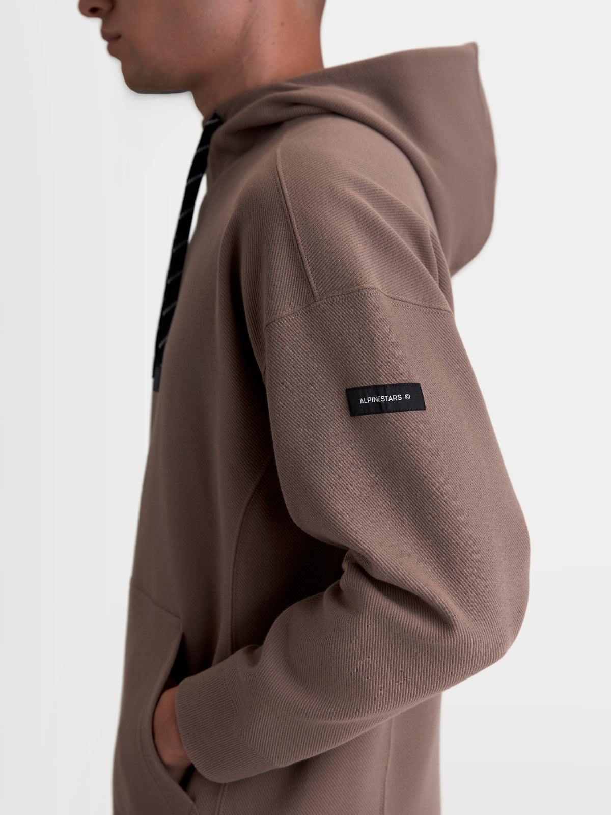 Alpinestars Camino Textured Oversized hoodie, casual sportswear-pullover, bruin taupe, zijaanzicht op model met gestructureerde knit twill fleece en geweven Alpinestars-label op de mouw
