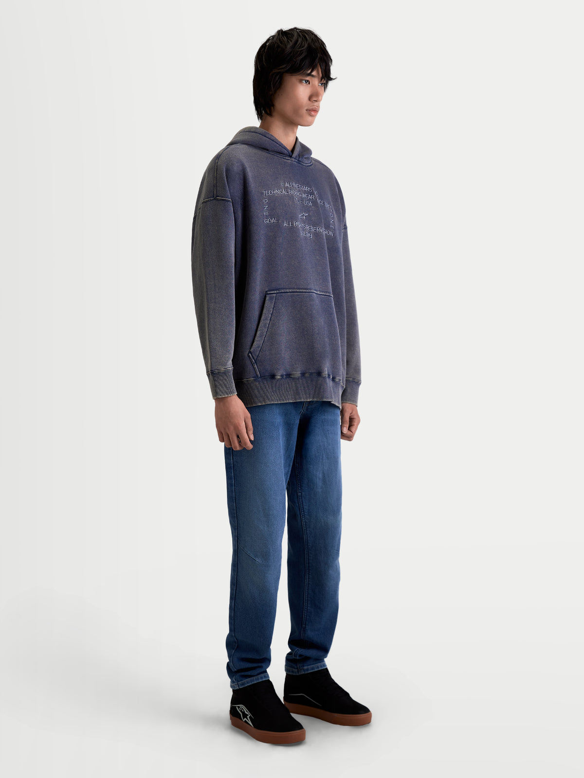 Alpinestars Infinite Washed Oversized Hoodie, sportswear lifestyle-pullover, unisex, gewassen donkerblauw, snow-wash fleece met een ontspannen pasvorm, kangoeroezak en geborduurde Alpinestars-branding, op model in een studio-opname