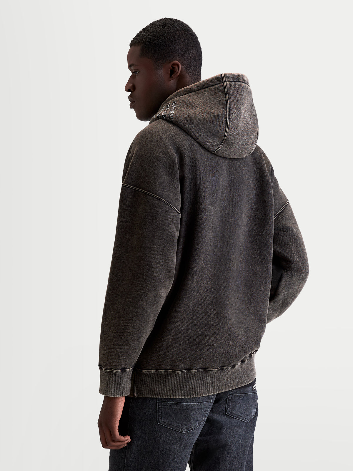 Alpinestars Infinite Washed Oversized Hoodie, herensportswear pullover, gewassen zwart, fleece met snow-wash afwerking, oversized pasvorm, gevoerde capuchon met geborduurd logo, achteraanzicht op model.