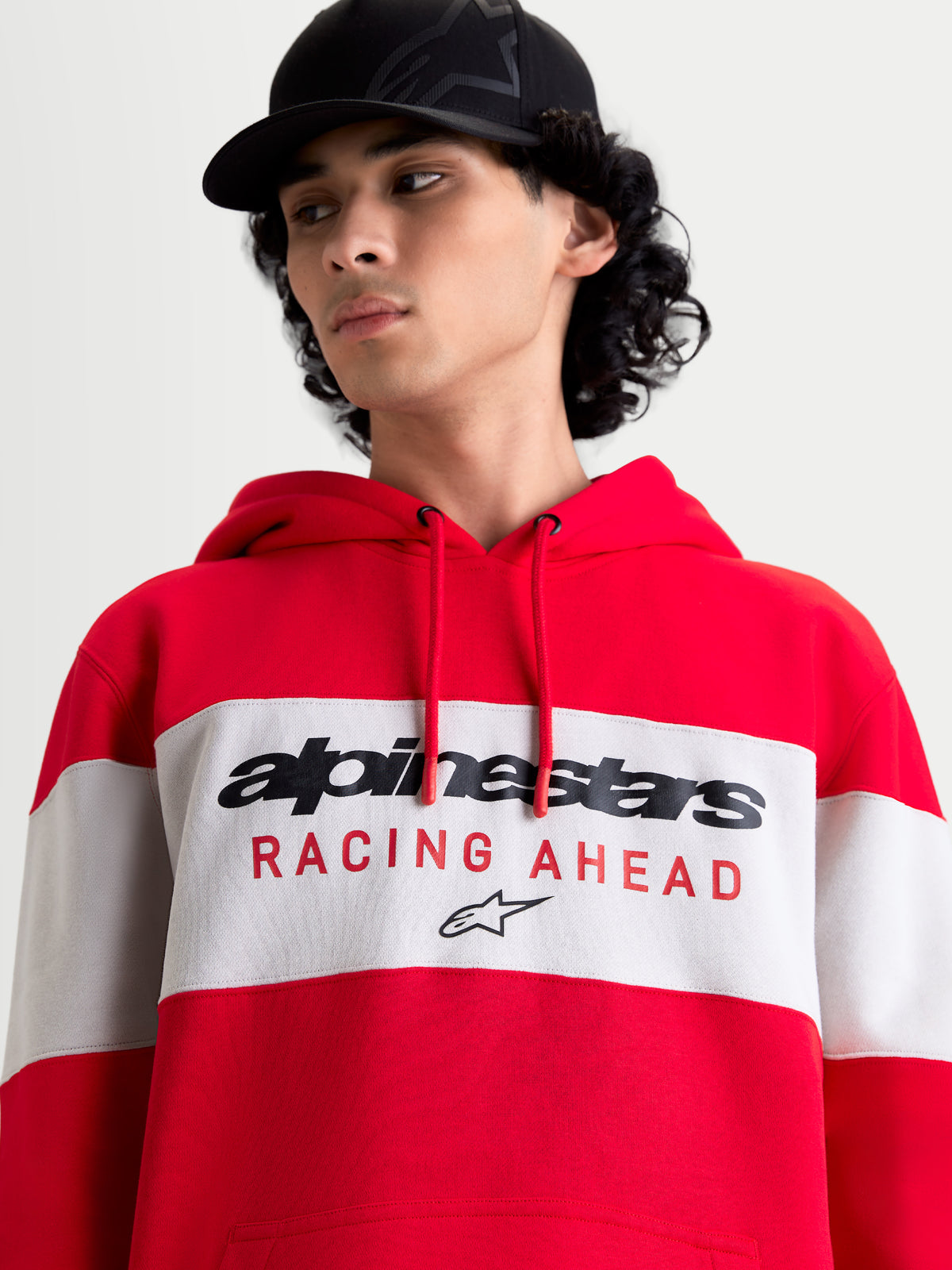 Alpinestars Cubic Hoodie, sportswear pullover hoodie, unisex, rood en wit, kleurgeblokt ontwerp met opvallend Alpinestars-logo en 'RACING AHEAD' grafisch ontwerp op de borst, zachte fleece van katoen en gerecycled polyester, op model.