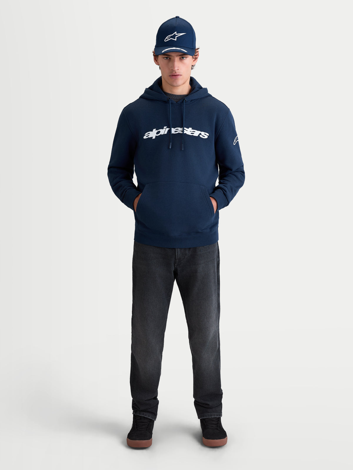 Alpinestars Race Wordmark Hoodie, sportswear pullover fleece, marineblauw en wit, met opvallend woordmerk op de borst en Ageless-logo op de mouw, lifestyle-weergave op model voor een casual motorsport-geïnspireerde look.