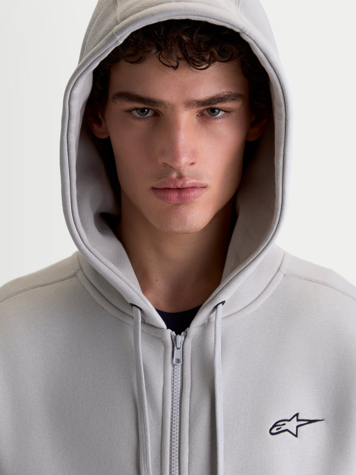 Alpinestars Entity Oversized Hoodie, sportswear fleece met ritssluiting, grijs, met Vislon-rits en geborduurd Astars-logo, close-up op een model met de capuchon omhoog.