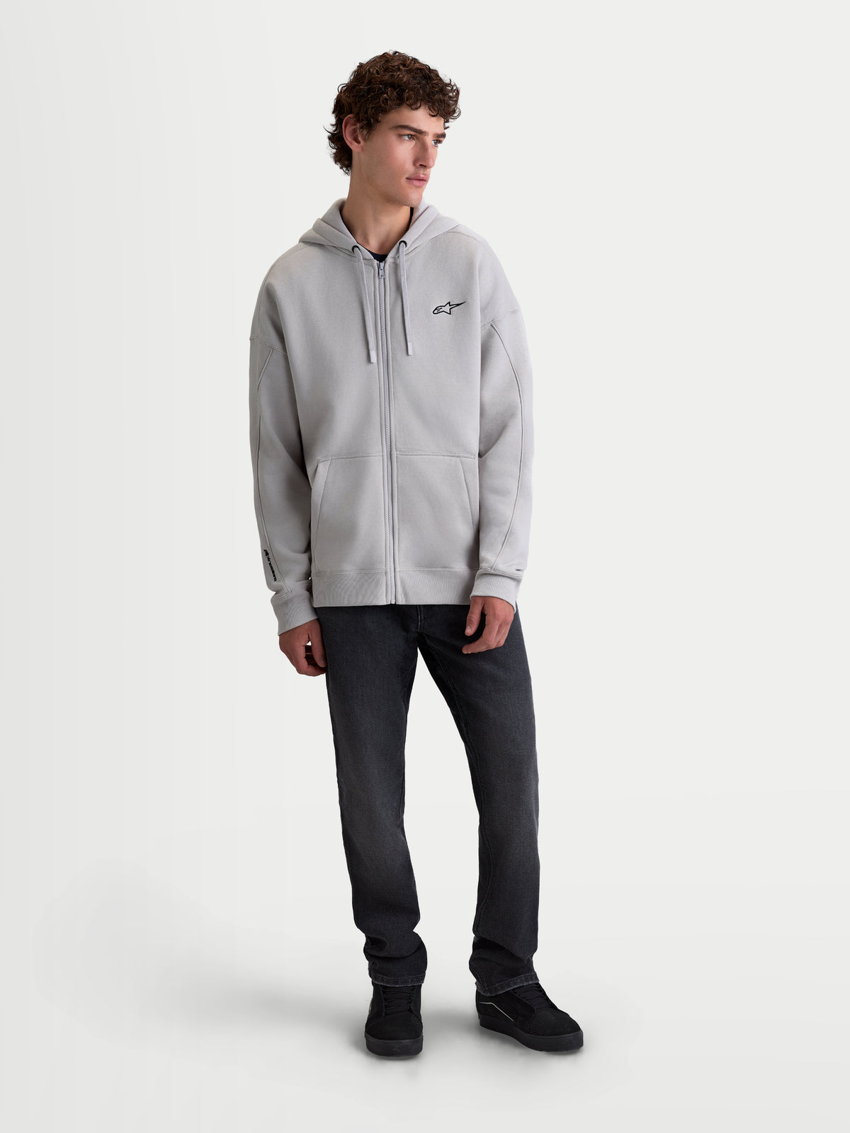 Alpinestars Entity Oversized Hoodie, grijze hoodie met ritssluiting, heren, premium katoenmix fleece met een relaxte oversized pasvorm, Vislon-rits aan de voorzijde, kangoeroezak en geborduurd logo op de borst, casual sportswear getoond op model.