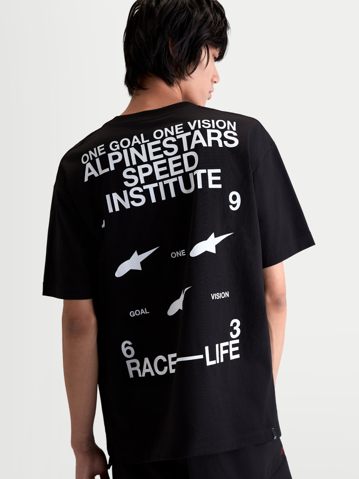 Alpinestars Institute Oversized CSF T-shirt, zwart en wit, achteraanzicht op model met Alpinestars Speed Institute en Race-Life graphics op de rug, relaxte oversized pasvorm, comfortabele katoen-polyester mix, casual sportswear.